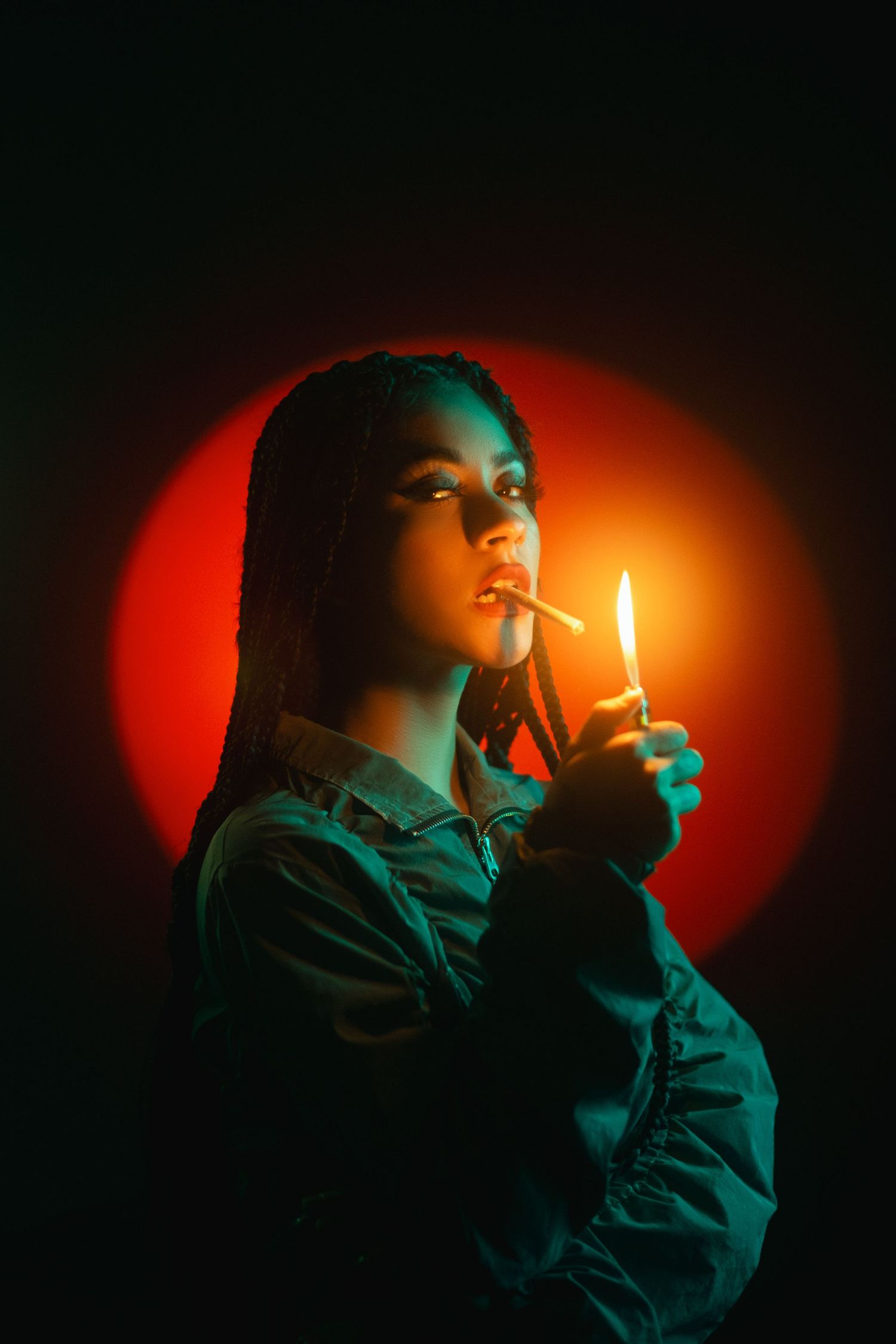 A figure stands in dramatic lighting with a red circle backdrop, illuminated by a lighter's glow in moody turquoise tones.