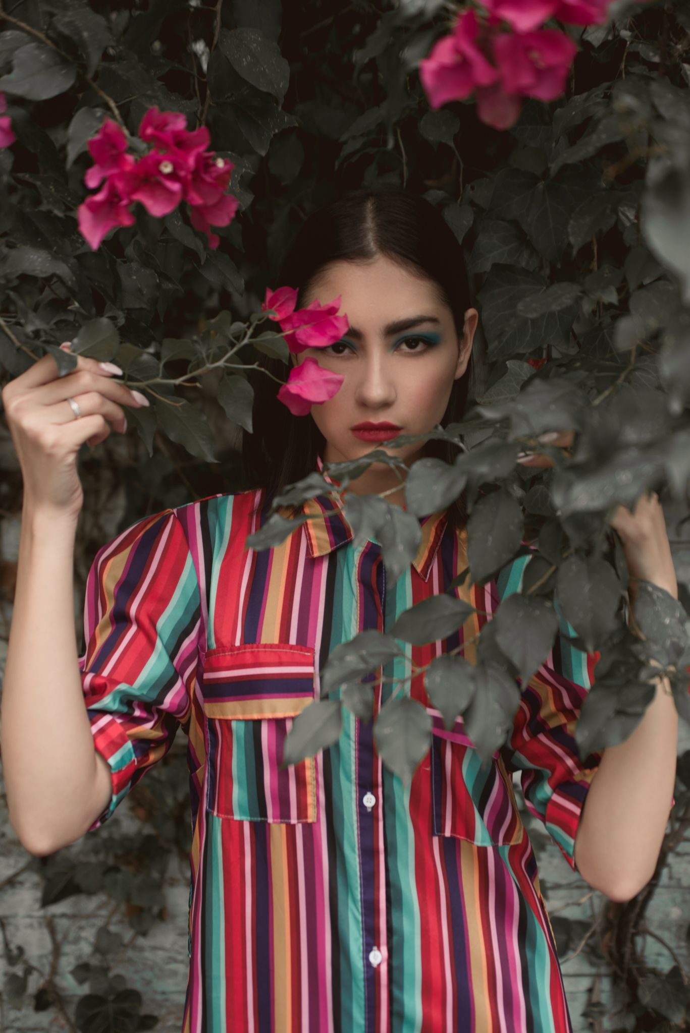 Fashion portrait among pink flowers wearing vibrant striped shirt.