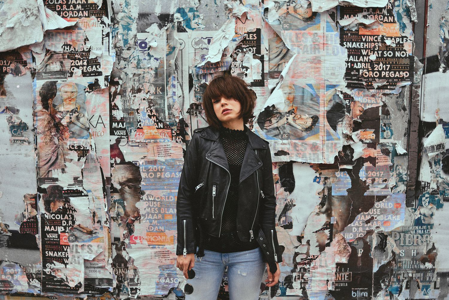 Street style portrait against backdrop of layered posters and graffiti.