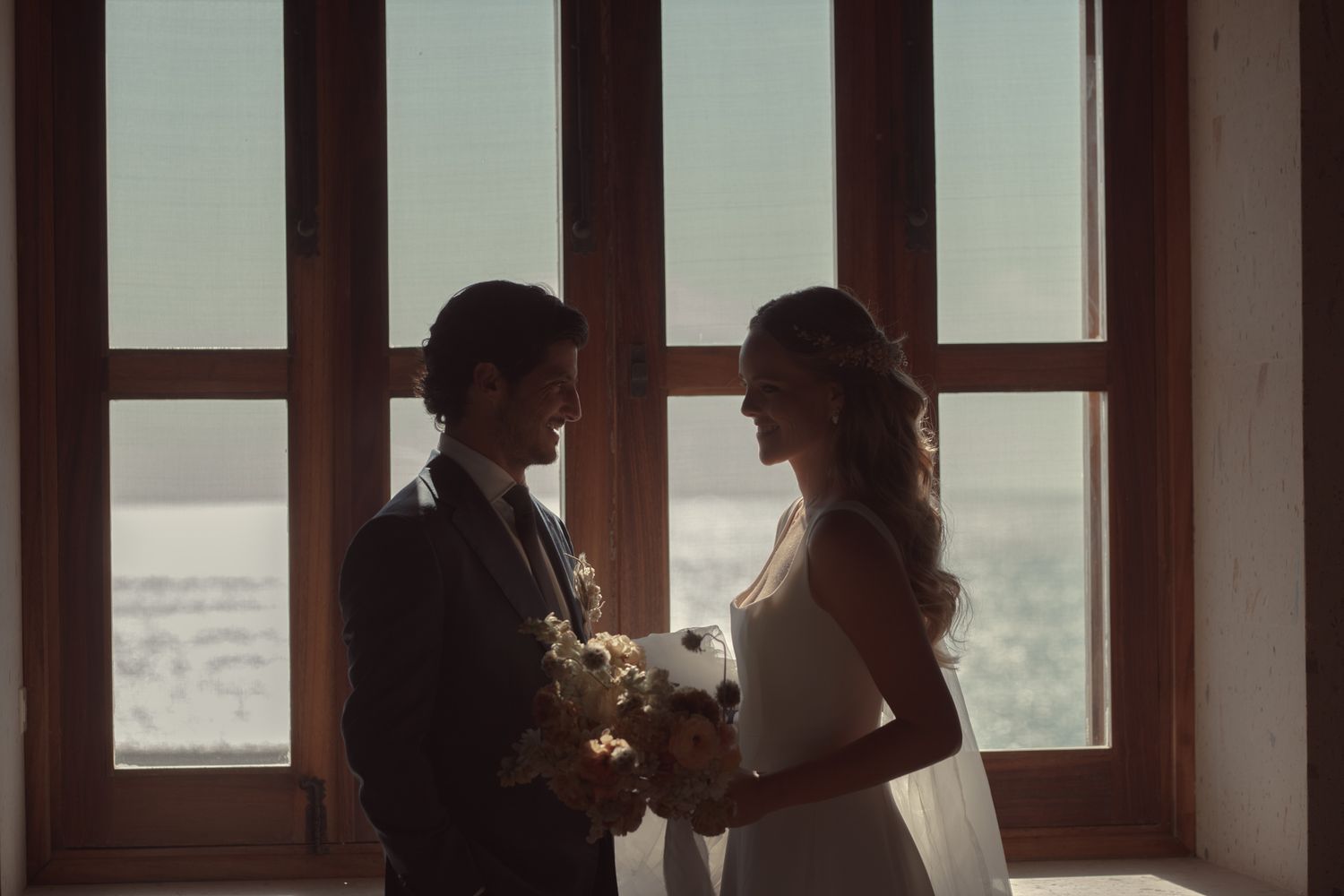 Romantic wedding scene with couple in silhouette against large window backdrop.