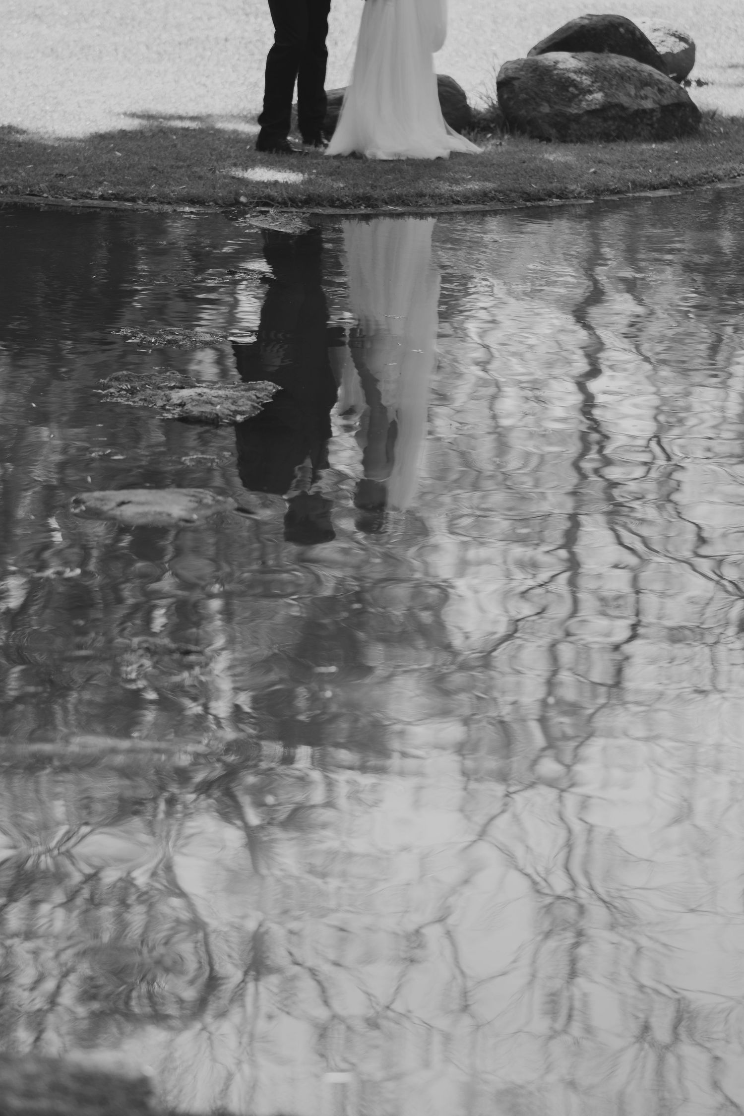 Artistic black and white reflection of wedding couple in water with distorted ripples.