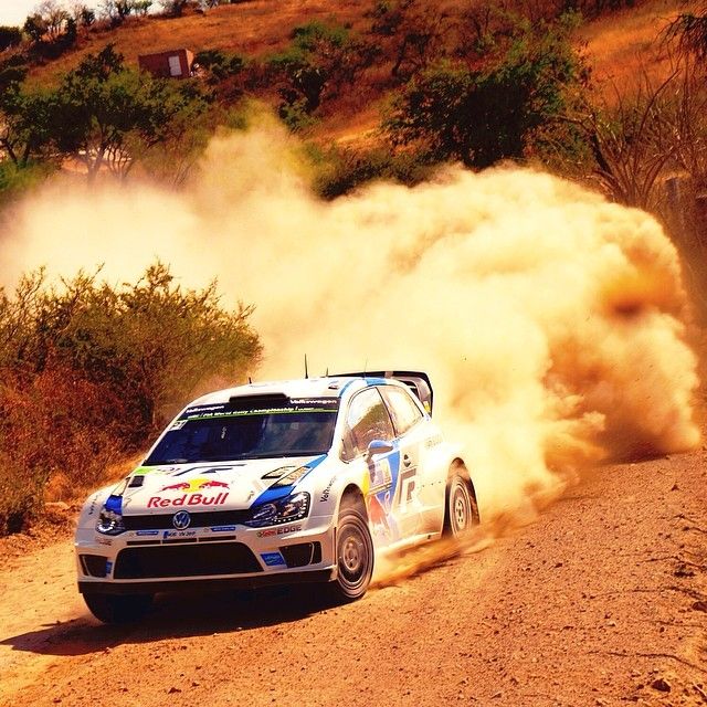 Rally cars kick up clouds of red dust while racing through a desert terrain during a competitive off-road event.