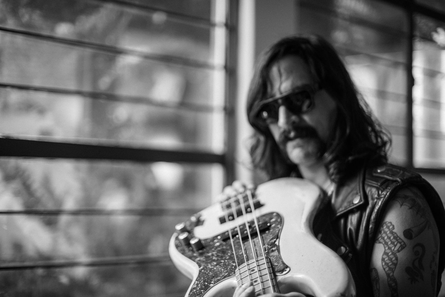 Close-up shot of musician playing electric bass guitar while wearing sunglasses and leather vest.