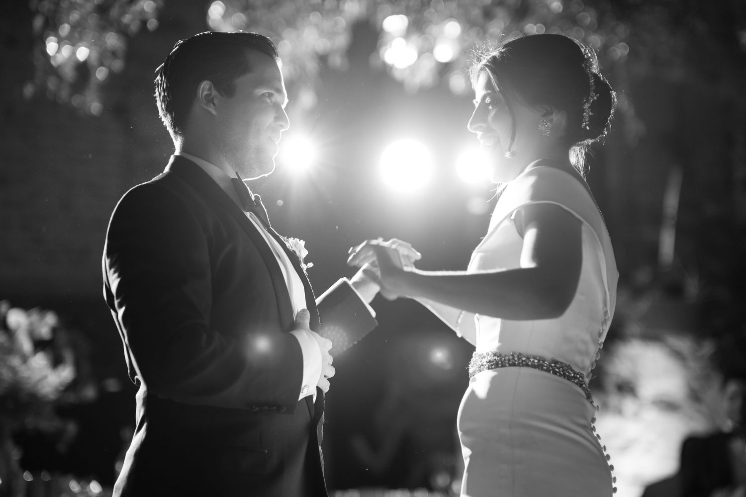 Intimate black and white portrait of couple dancing under evening lights at reception.