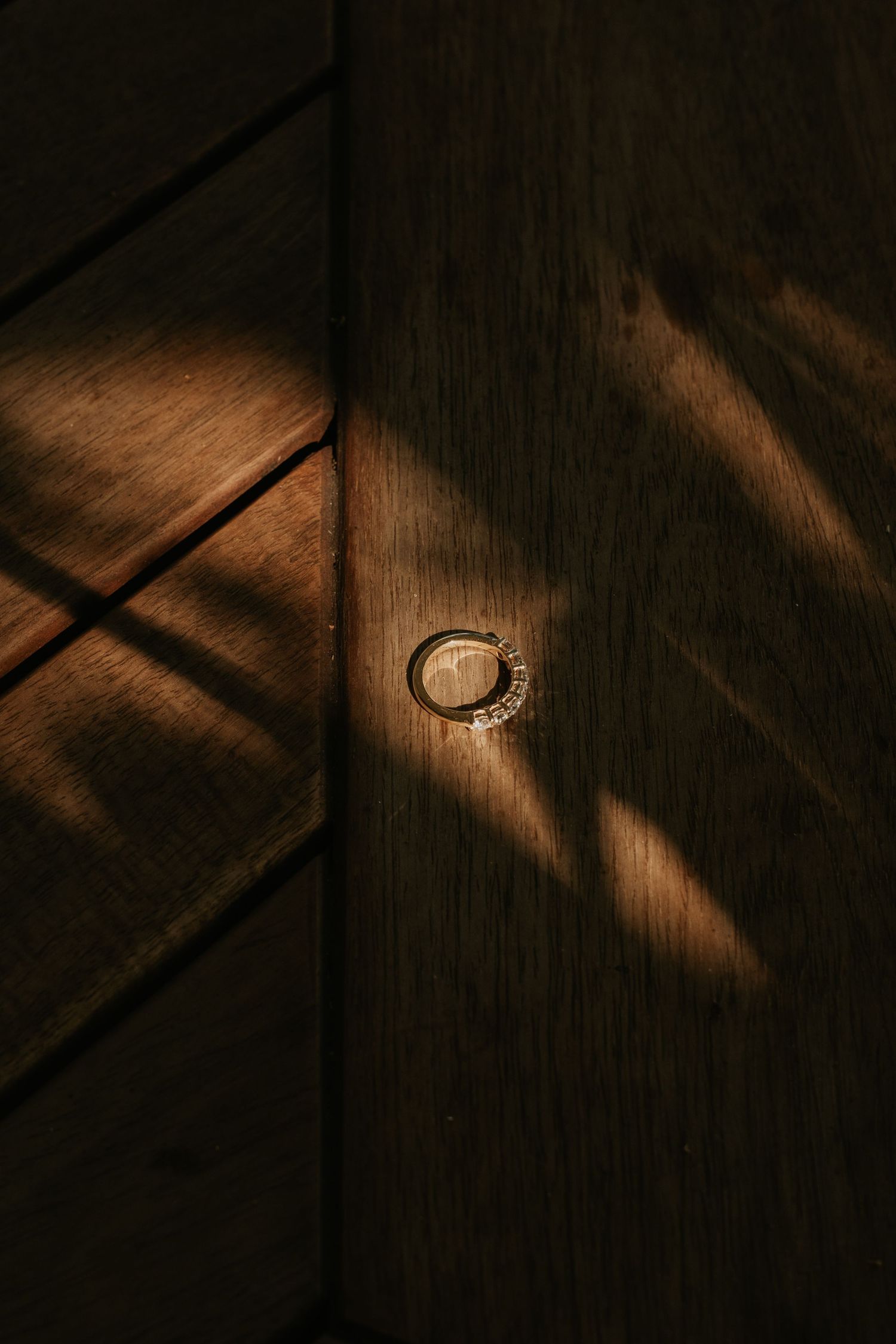 Wedding rings on wooden surface with dramatic diagonal shadow lines.