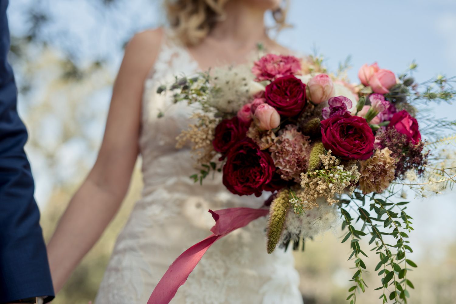 Elegant wedding bouquet with deep red roses, pink flowers and trailing greenery with silk ribbon.