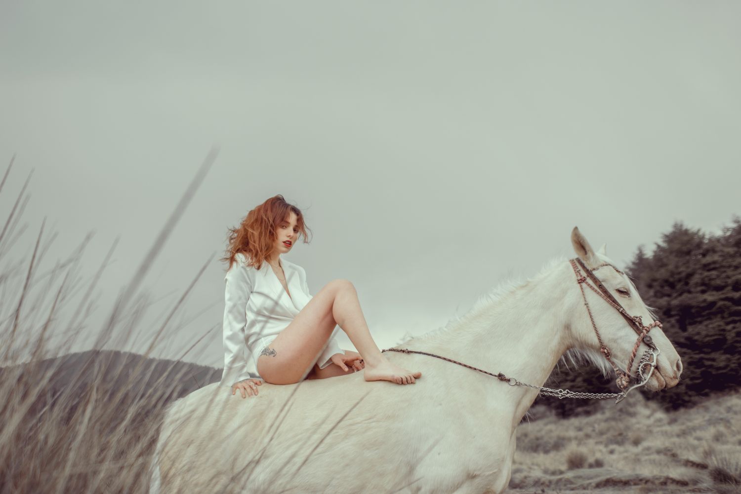 Woman in white sitting bareback on a white horse against moody sky.