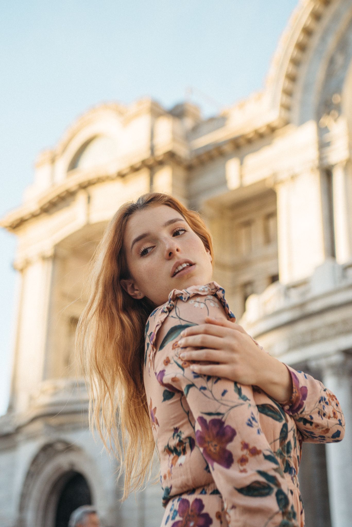 Artistic fashion portrait in floral dress against classical architecture backdrop.