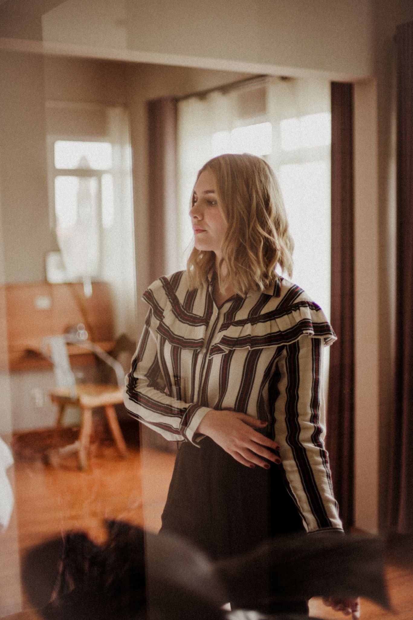 Sunlit interior portrait in striped shirt by window with warm vintage tones.