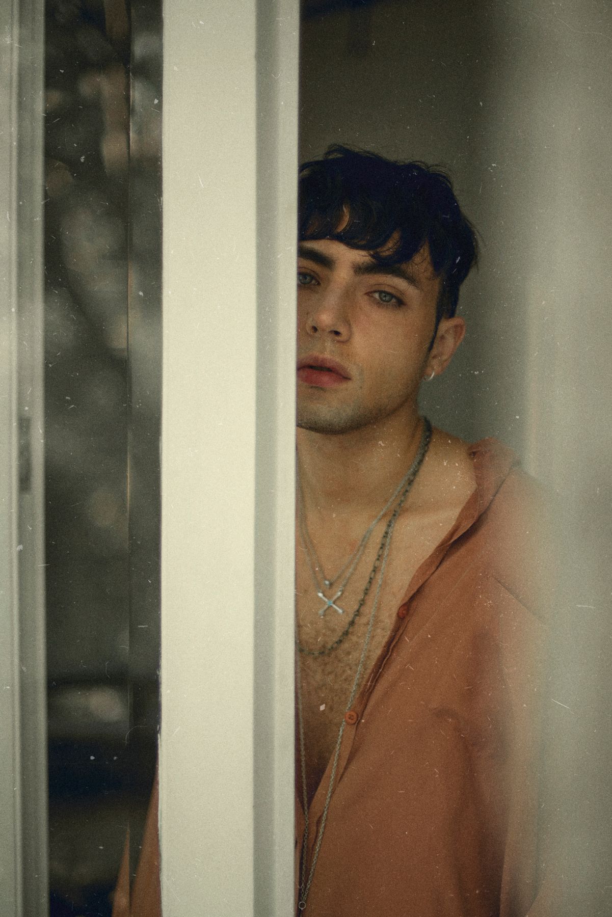 Moody portrait through window frame in soft natural lighting.