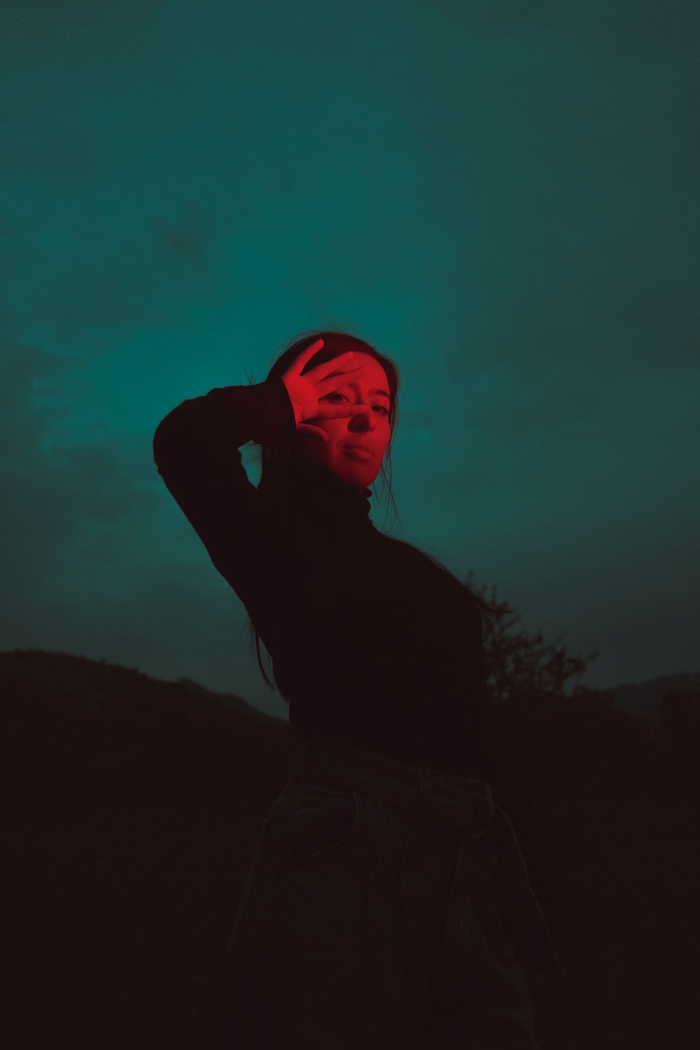 Silhouette against turquoise sky with red lighting creating mysterious mood.
