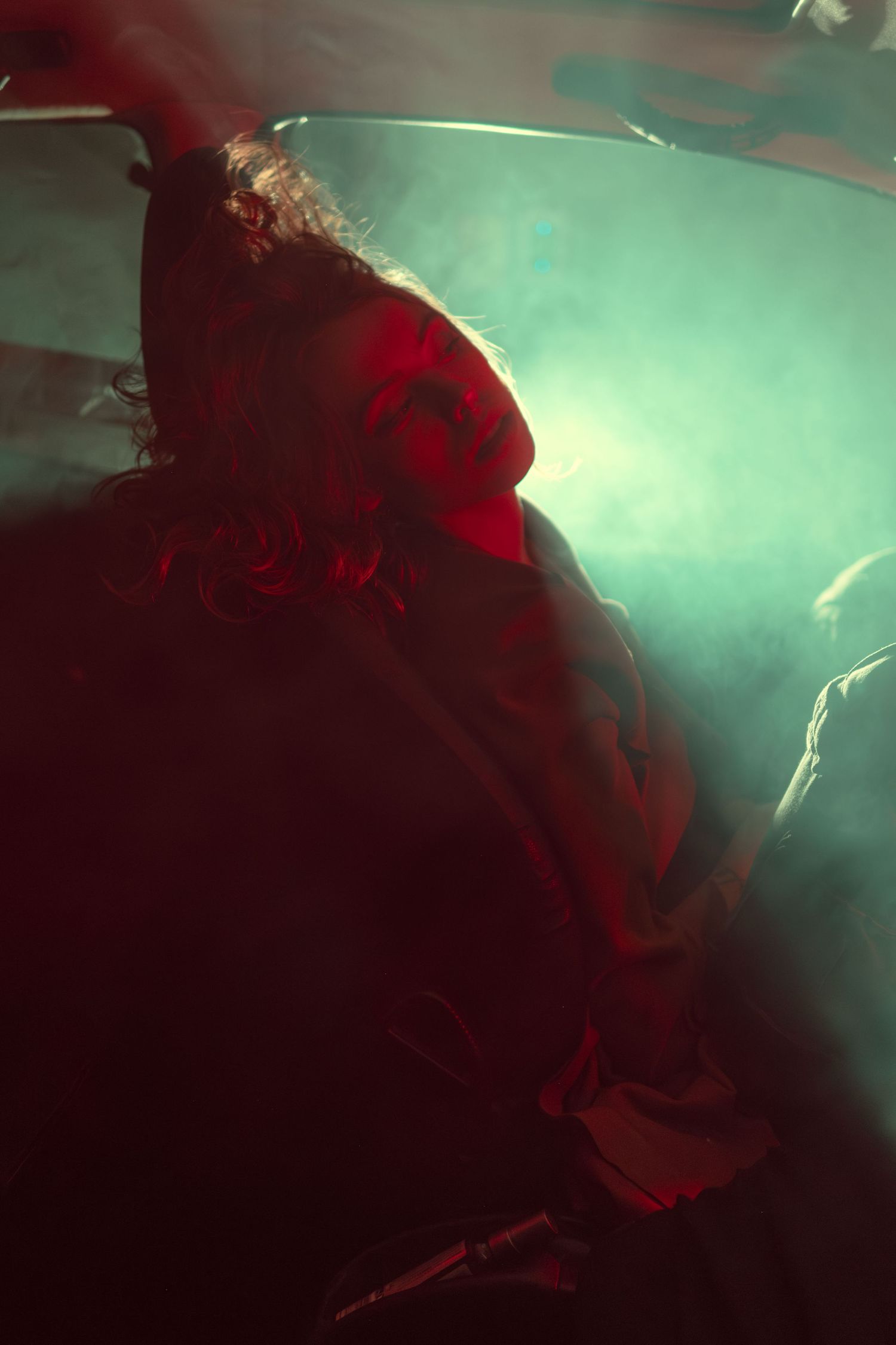 Figure in red lighting sits in atmospheric hazy green background creating moody cinematic ambiance.