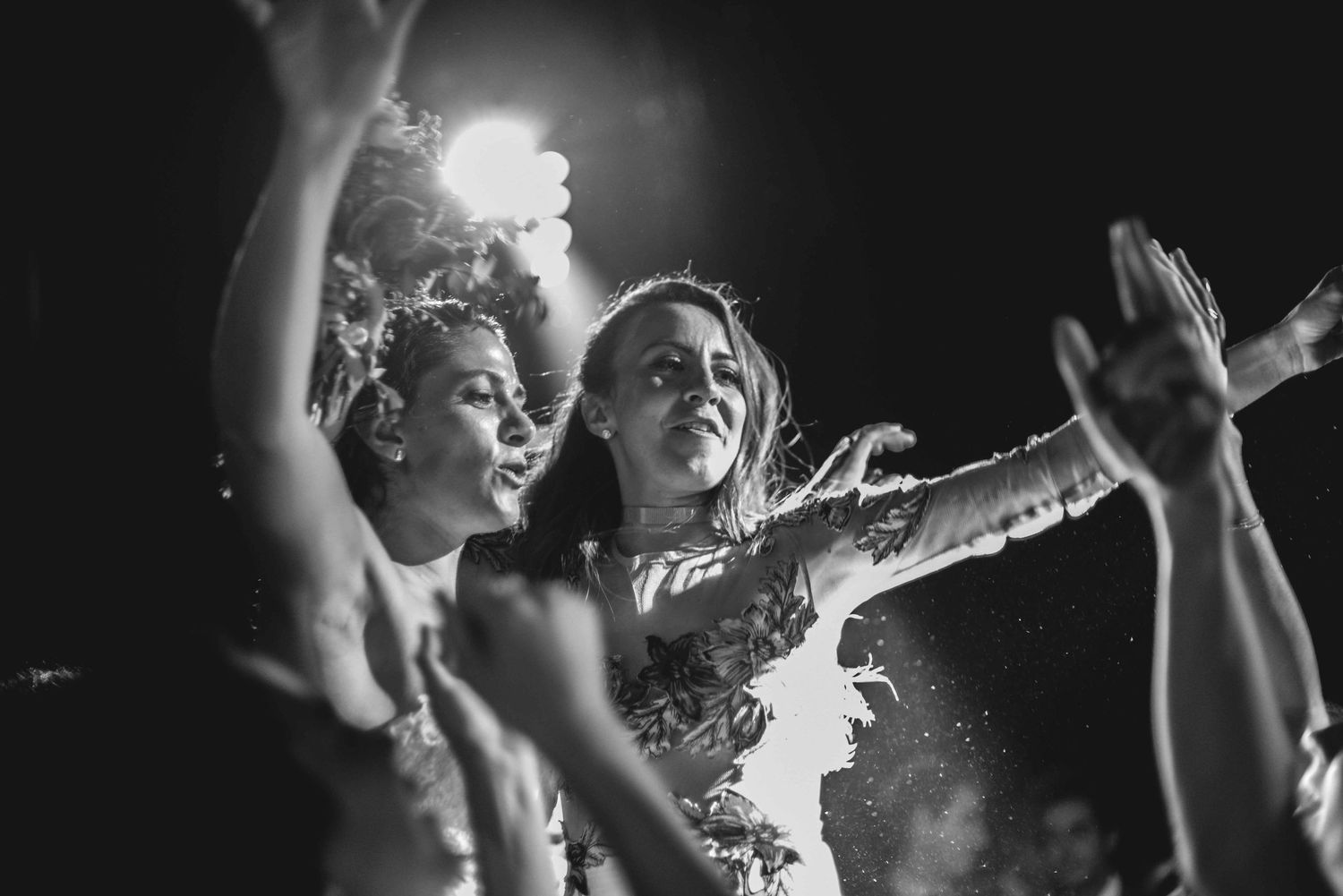 A black and white photo shows concert attendees dancing with their arms raised at a nighttime event.