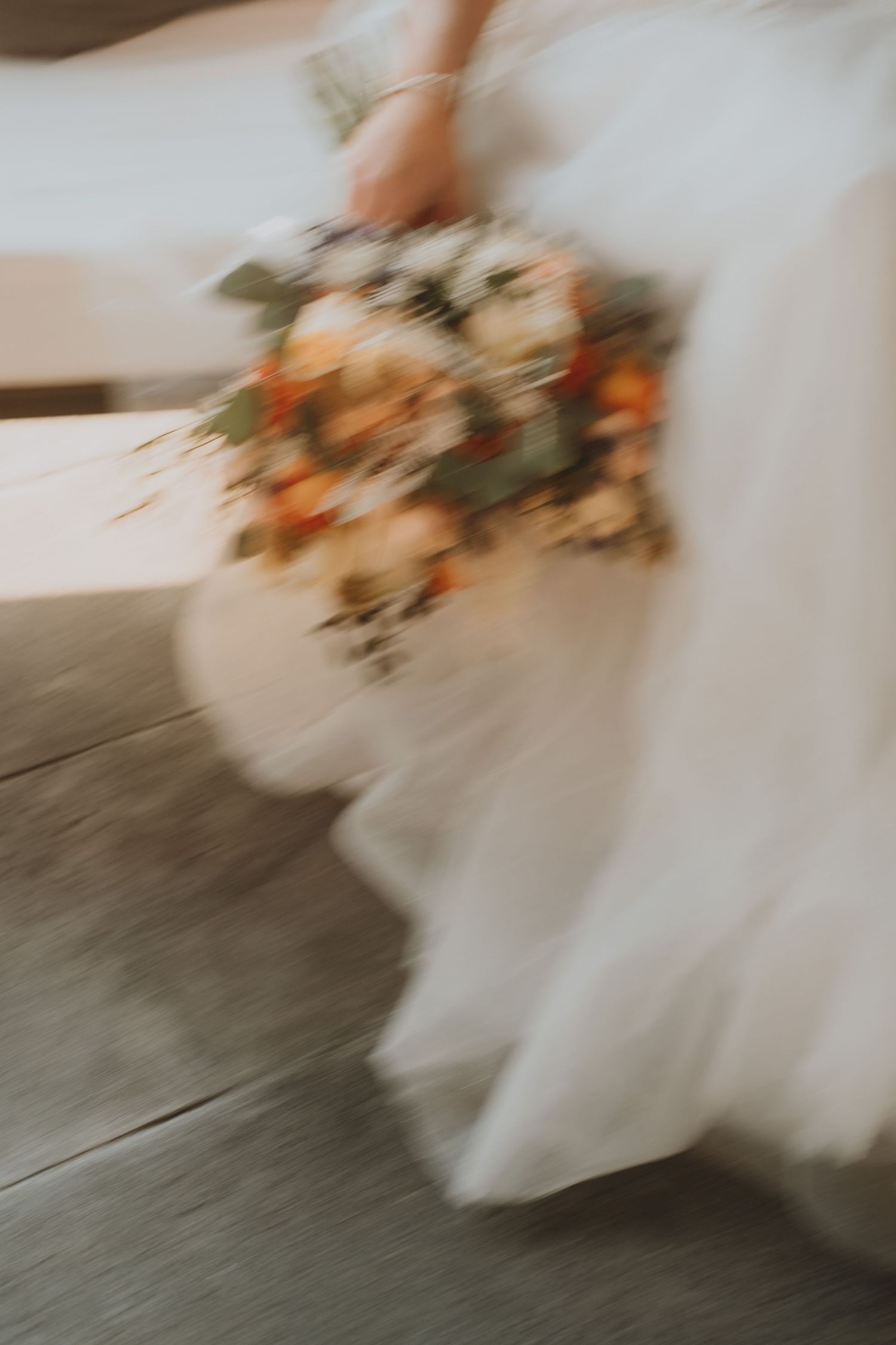 Artistic close-up of a wedding dress and peach-colored bouquet on hardwood floors.