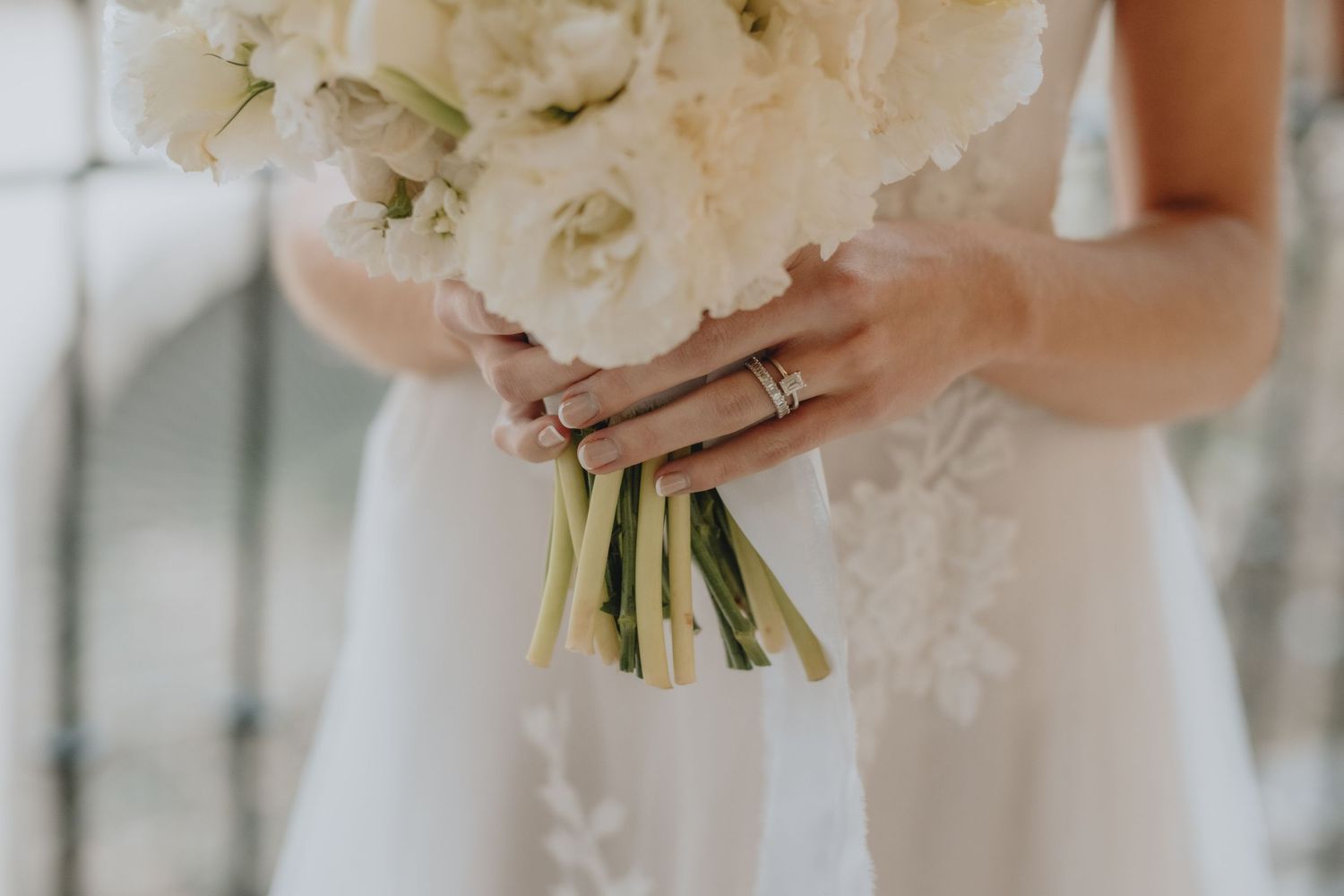 Close-up of bridal bouquet with white flowers and wedding rings visible on the bride's hand.