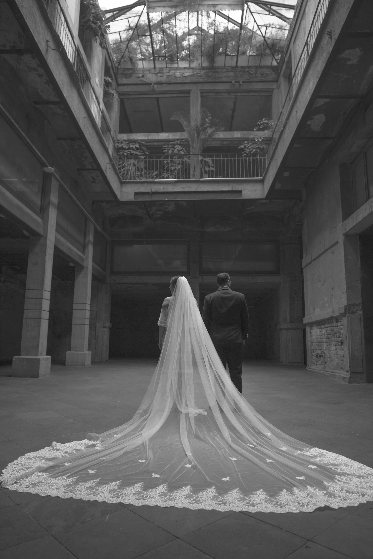 Dramatic black and white photo of a cathedral-length lace veil trailing behind newlyweds.