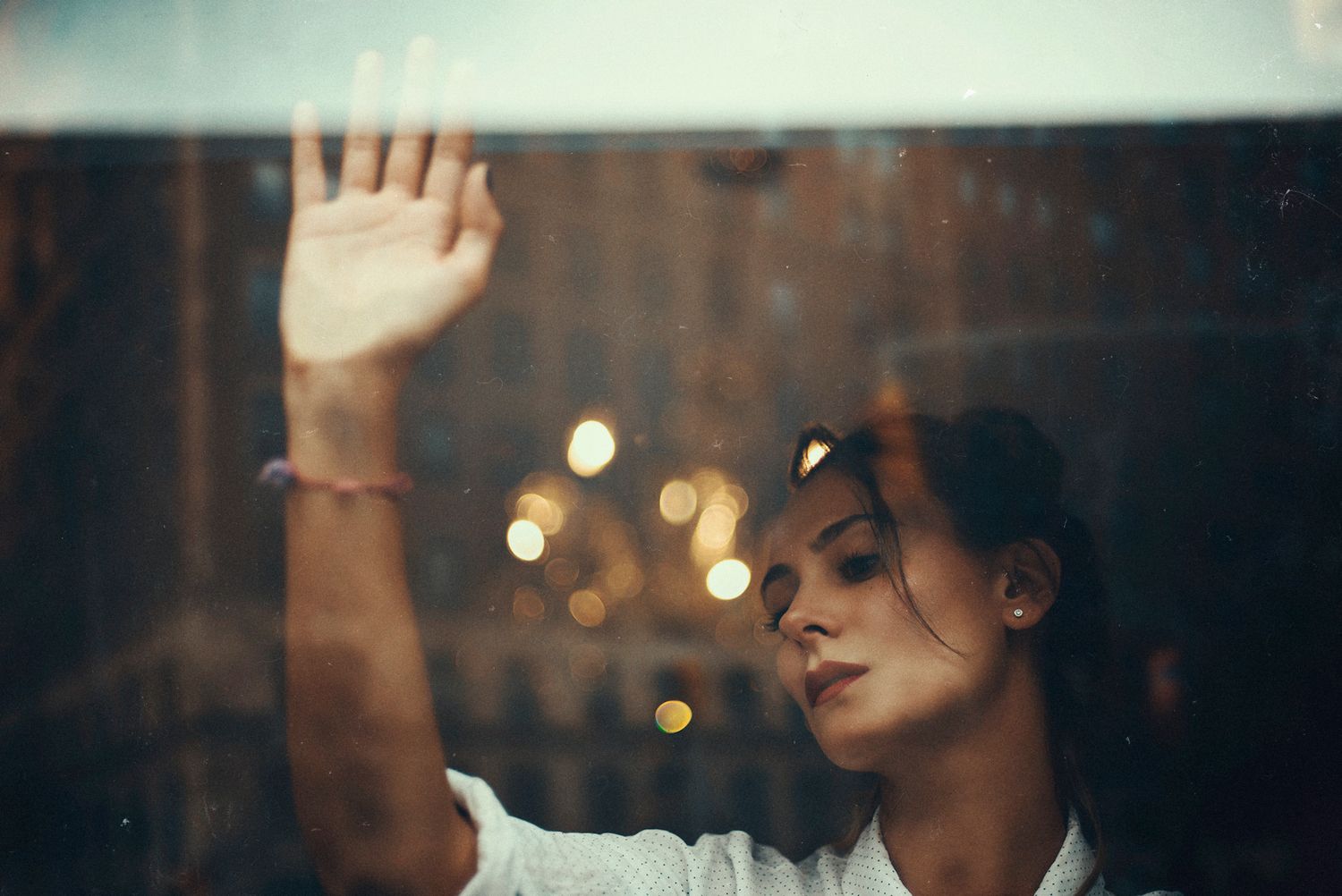 Artistic shot through glass with palm pressed against window and bokeh lights.