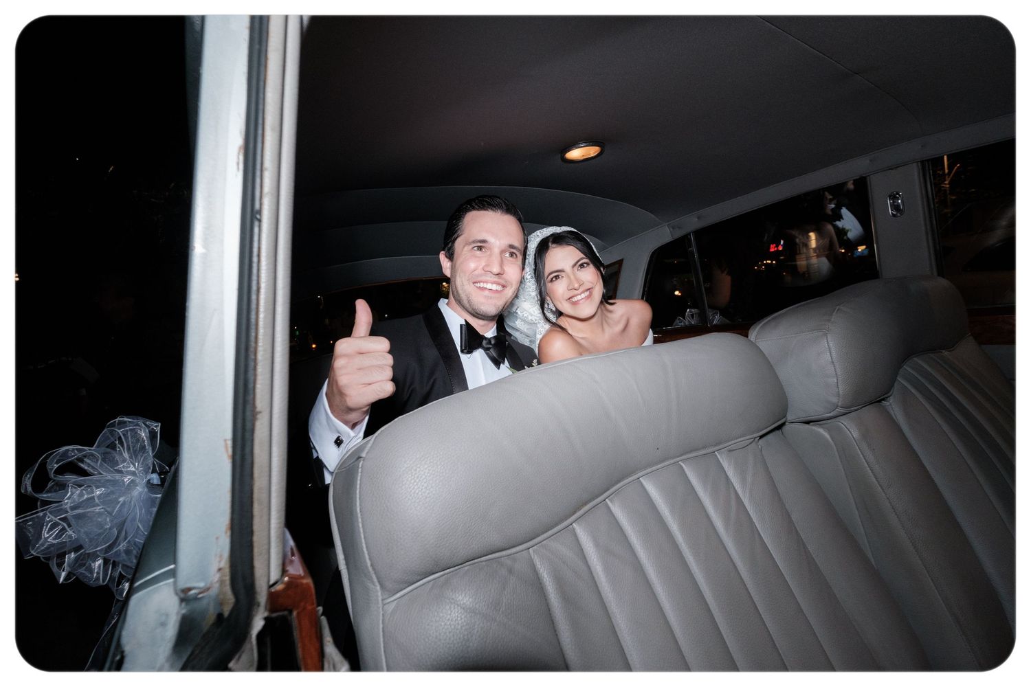Happy couple gives thumbs up while seated in the back of a wedding limousine.