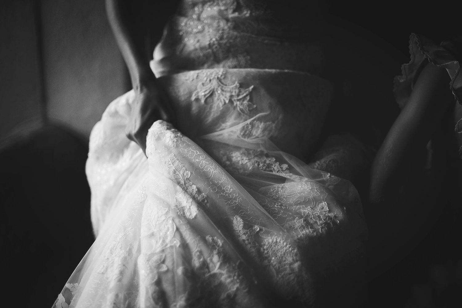 A close-up black and white shot of delicate lace details on an elegant wedding dress.