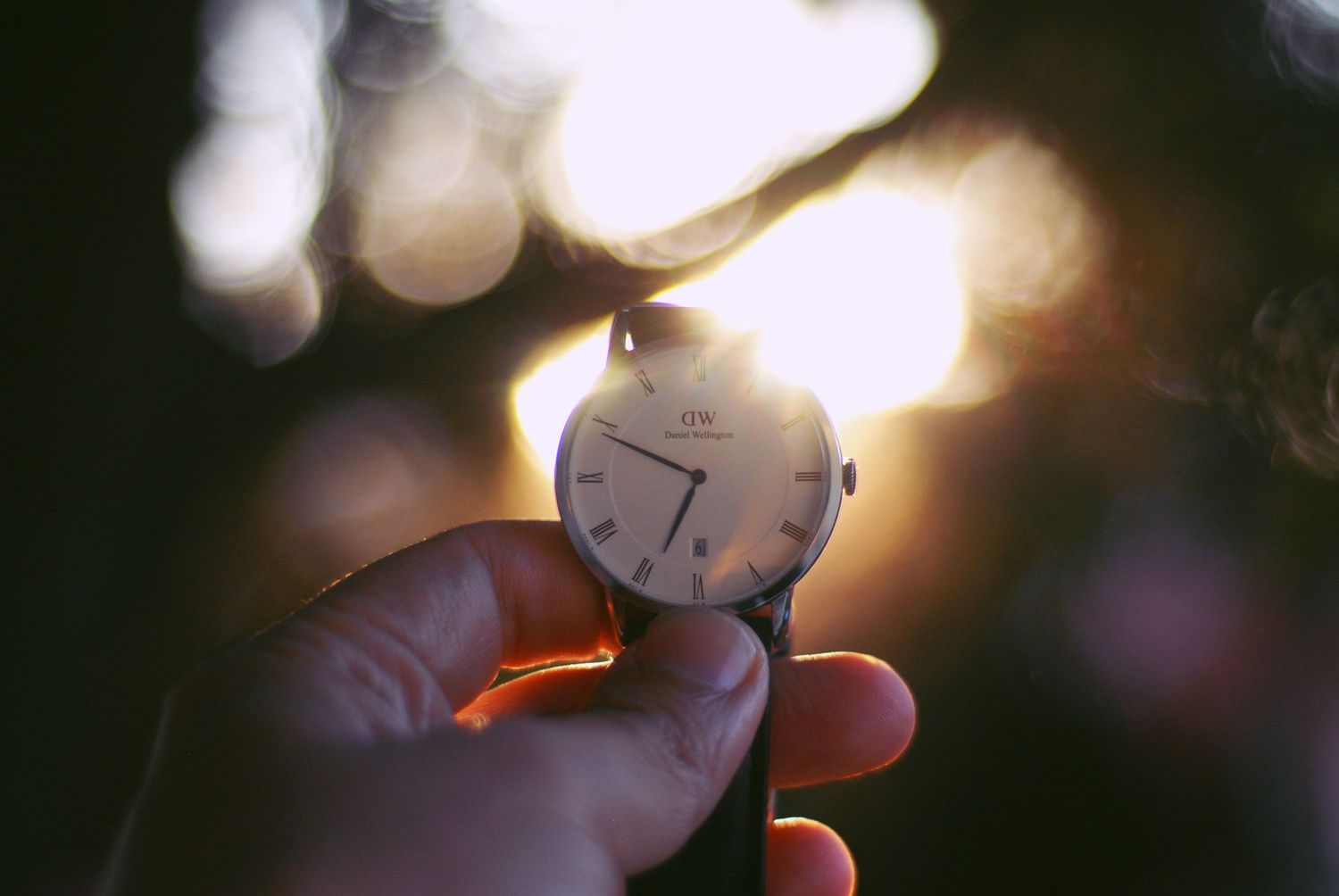 A dreamy soft-focus image of clock hands lit by golden bokeh lights at dusk.