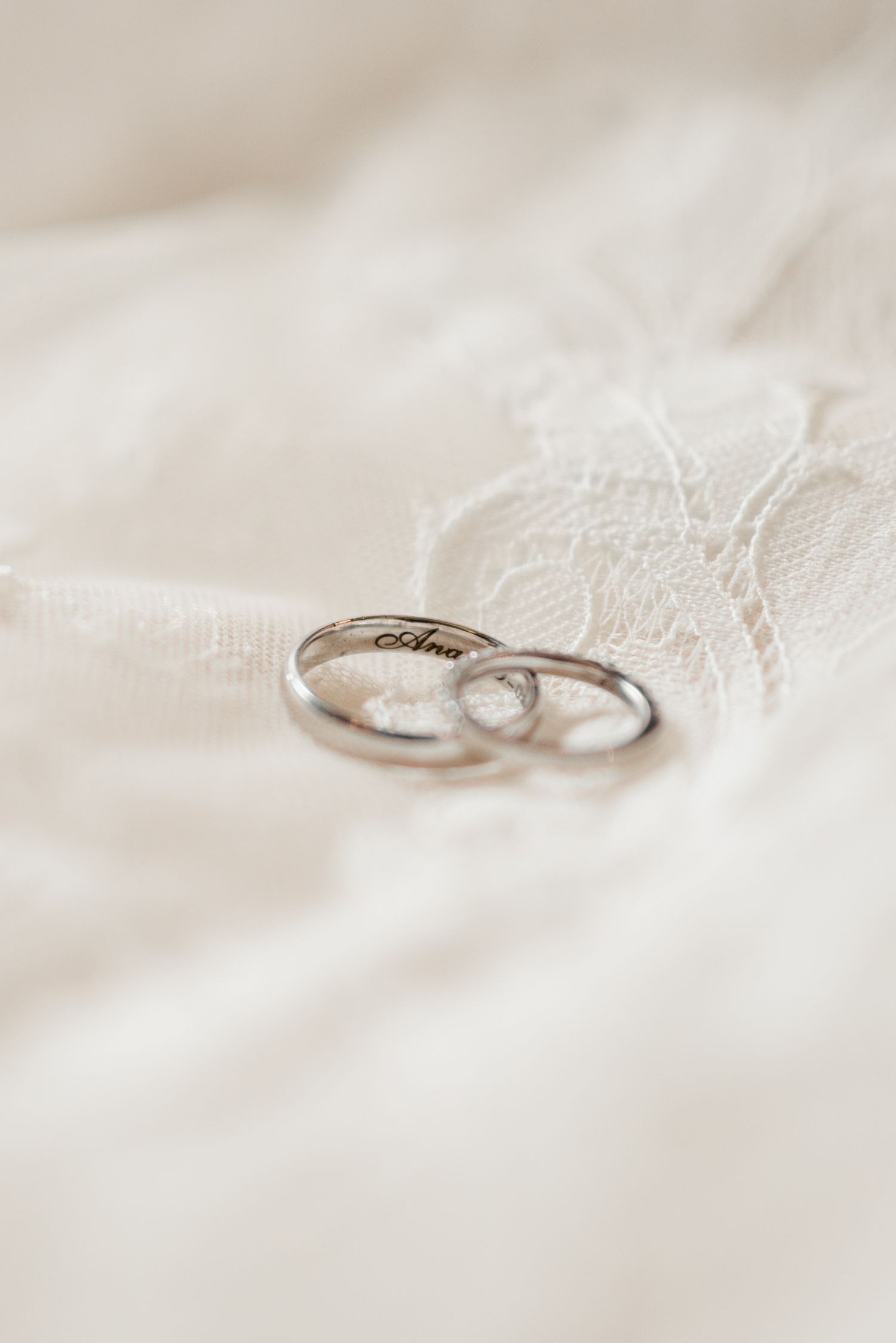 Two silver wedding rings resting on delicate white lace fabric with soft neutral background.