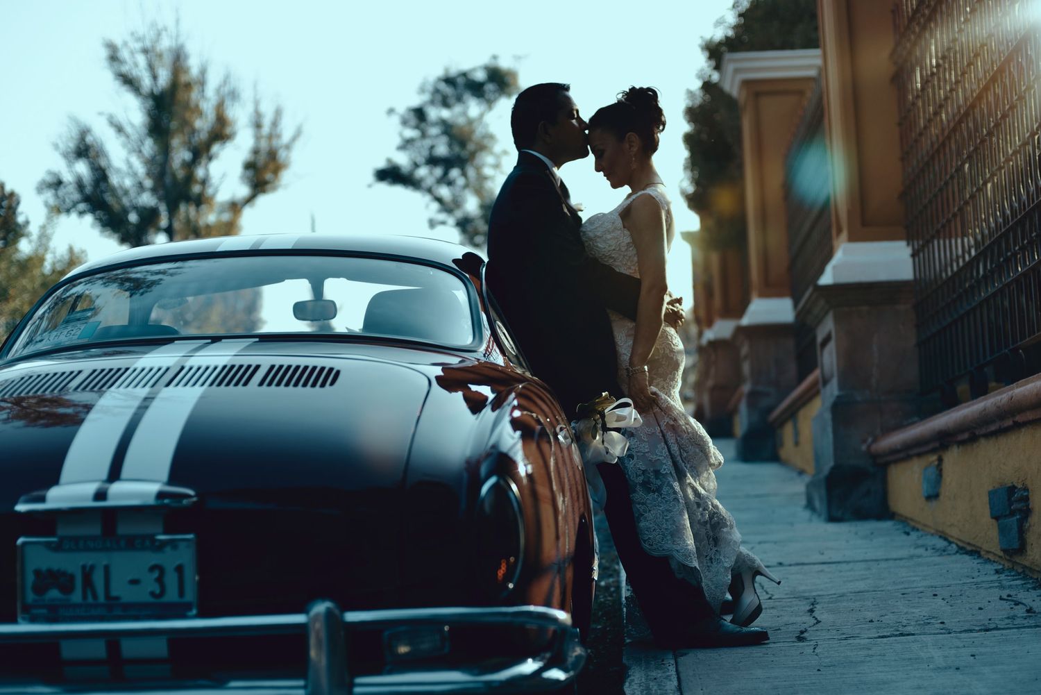 A vintage black car with racing stripes parked on a hill as a couple shares a romantic moment at sunset.