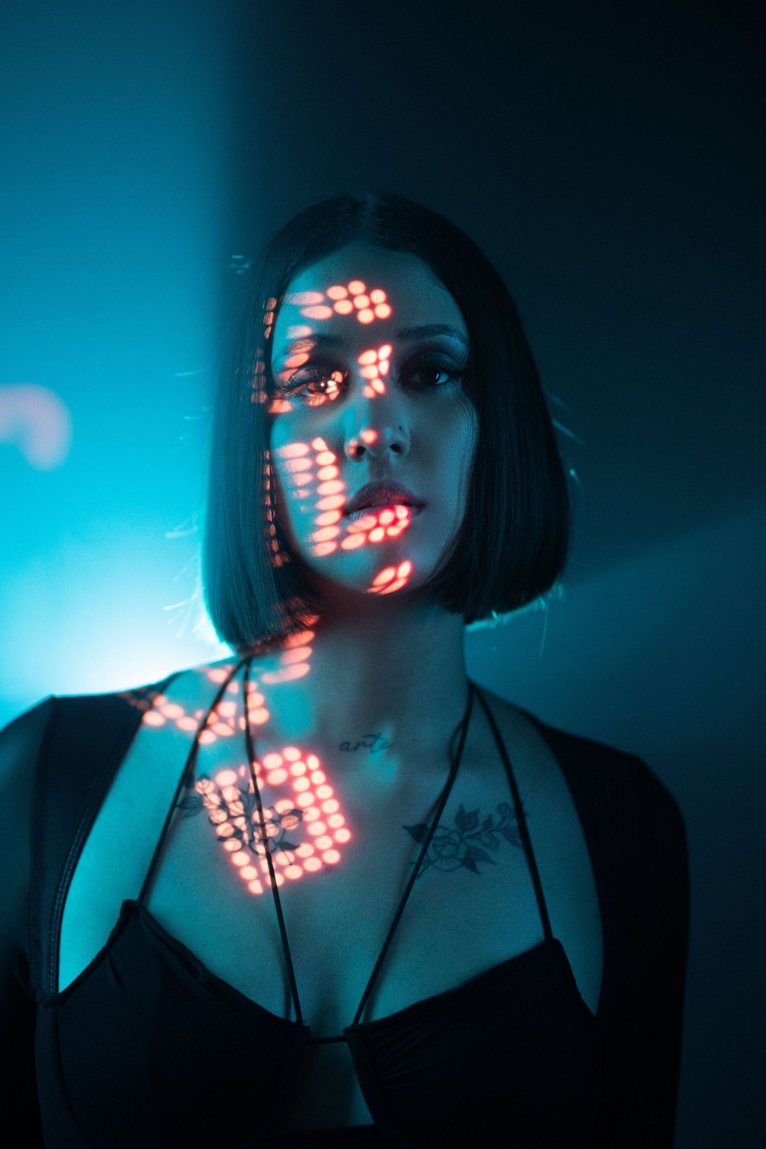 Artistic portrait with red neon light patterns projected onto subject against moody blue background in dark setting.