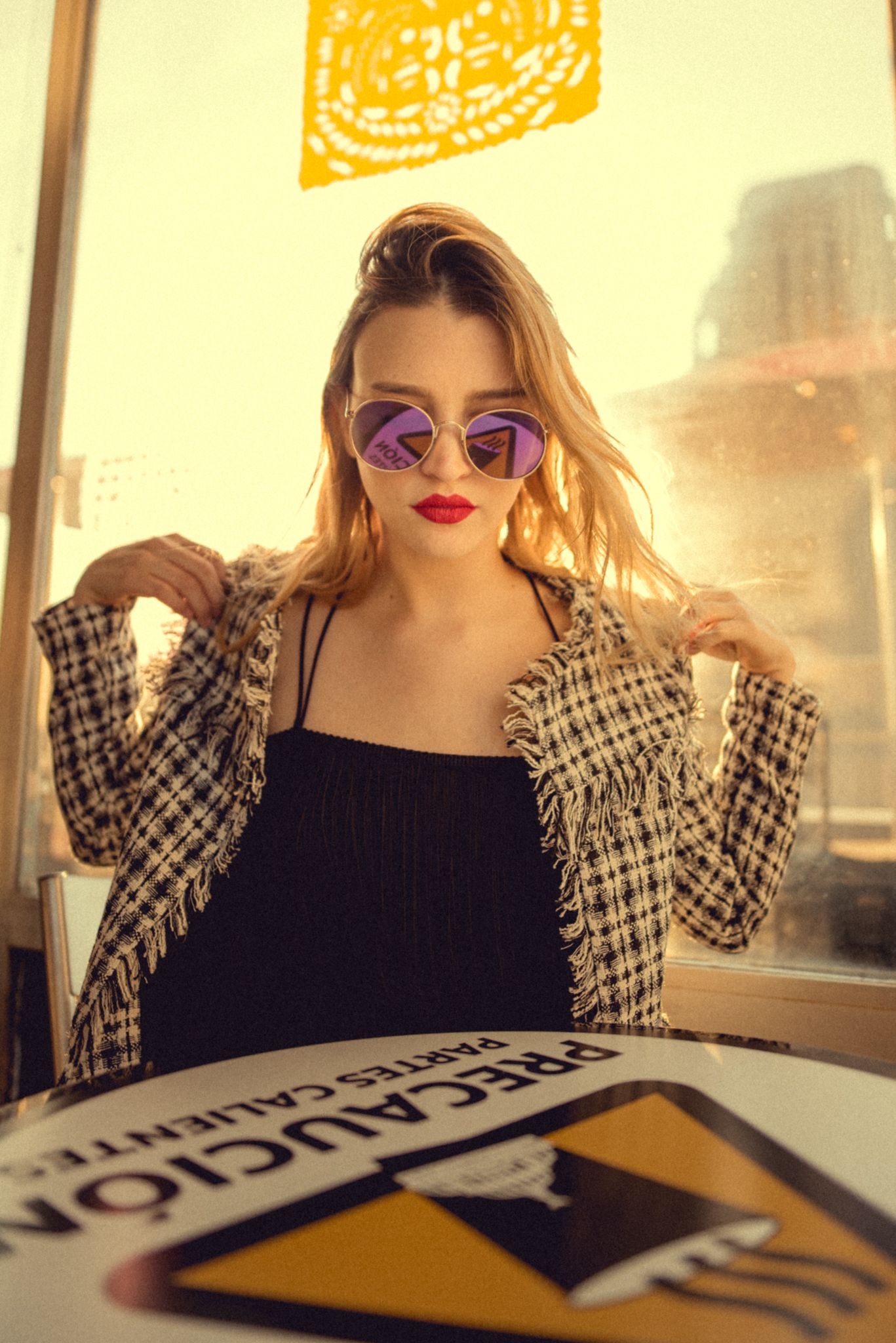 Retro-inspired fashion portrait with plaid jacket and purple sunglasses in warm lighting.