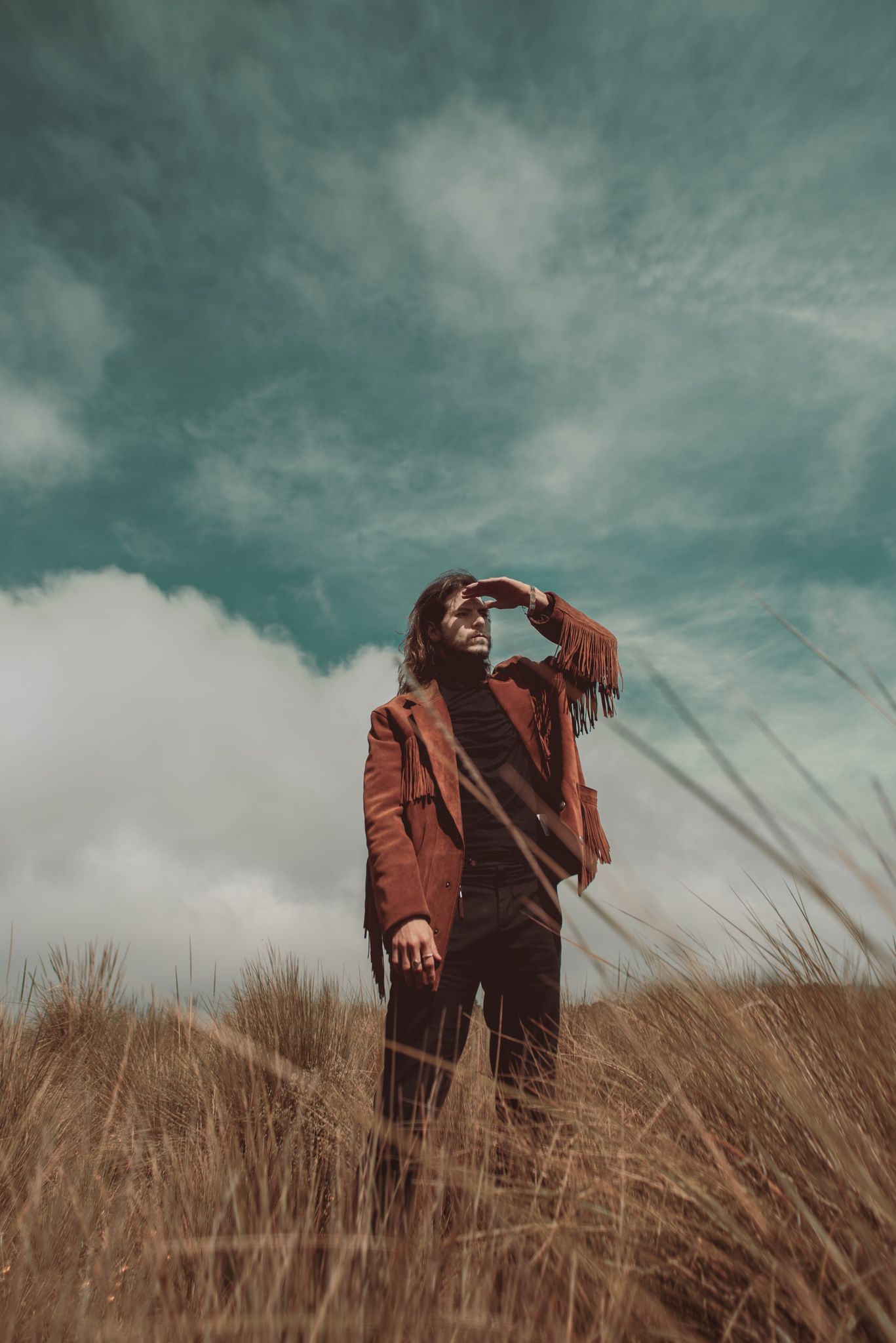 Person in brown jacket shielding eyes in sunlit golden field.