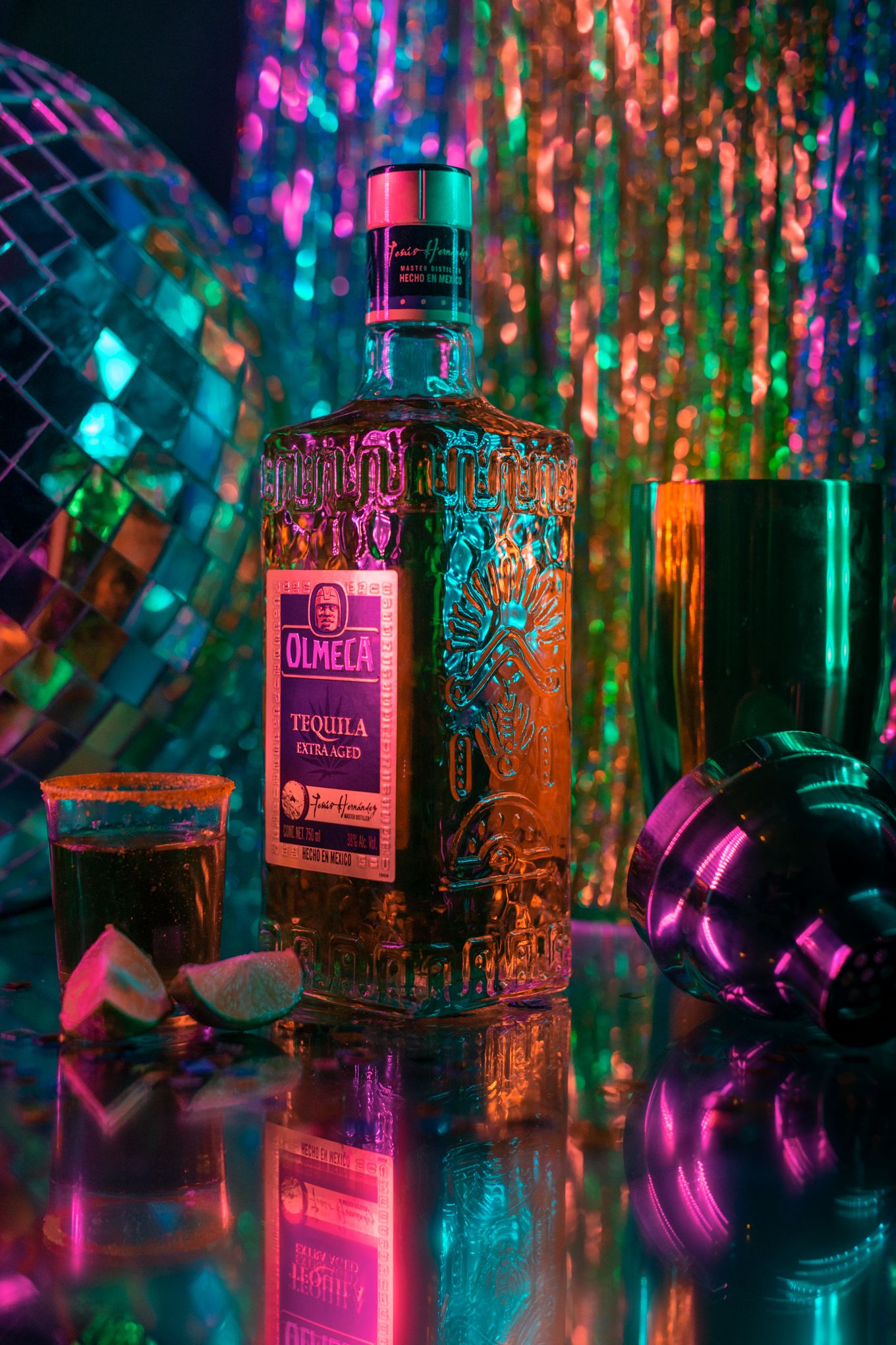 Ornate liquor bottle with disco ball against colorful sparkly backdrop.