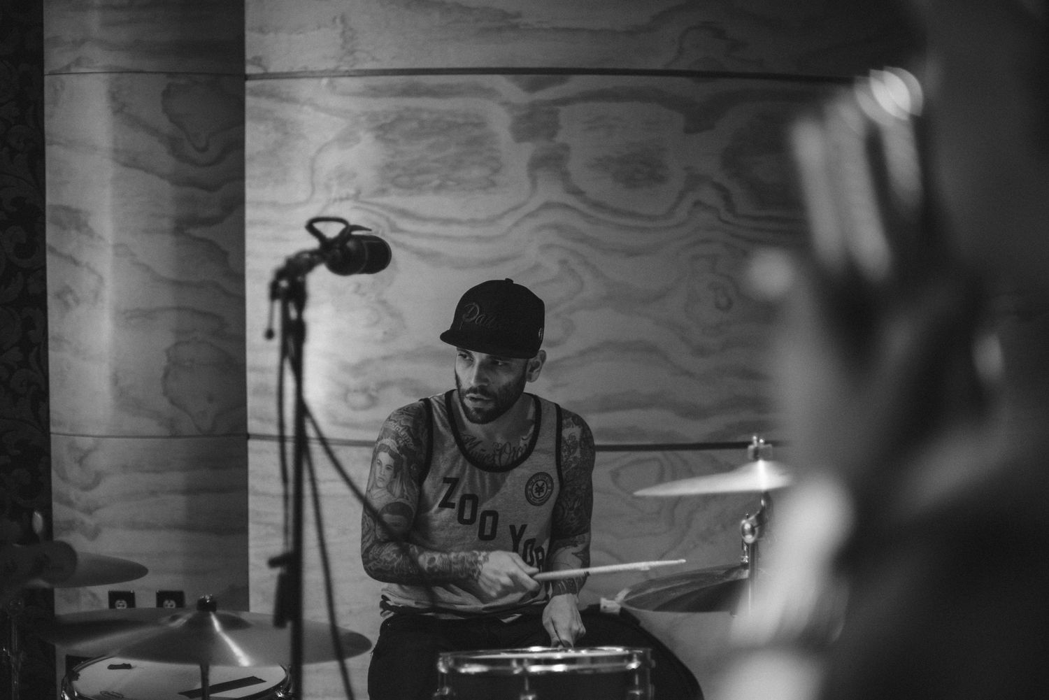 Black and white photo of a musician performing behind drums with studio lighting.