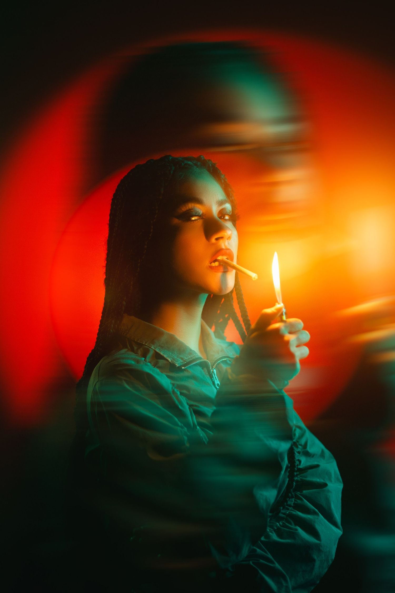 Artistic portrait with dramatic red and turquoise lighting features someone lighting a cigarette with a handheld lighter.
