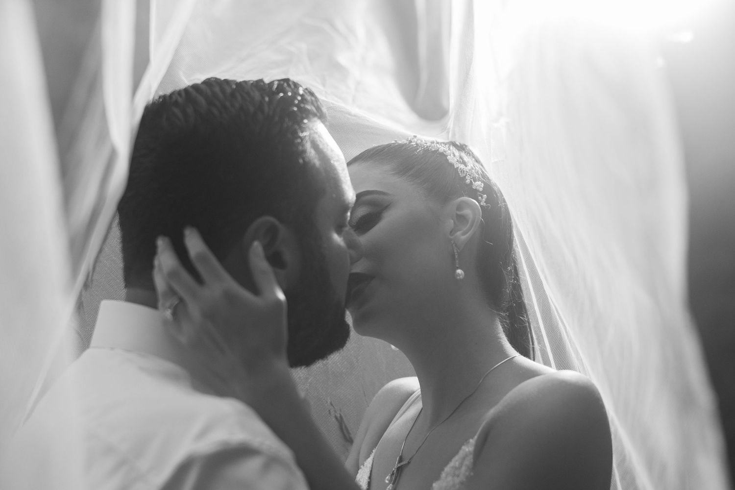 An intimate black and white portrait of newlyweds sharing a tender moment under a veil.