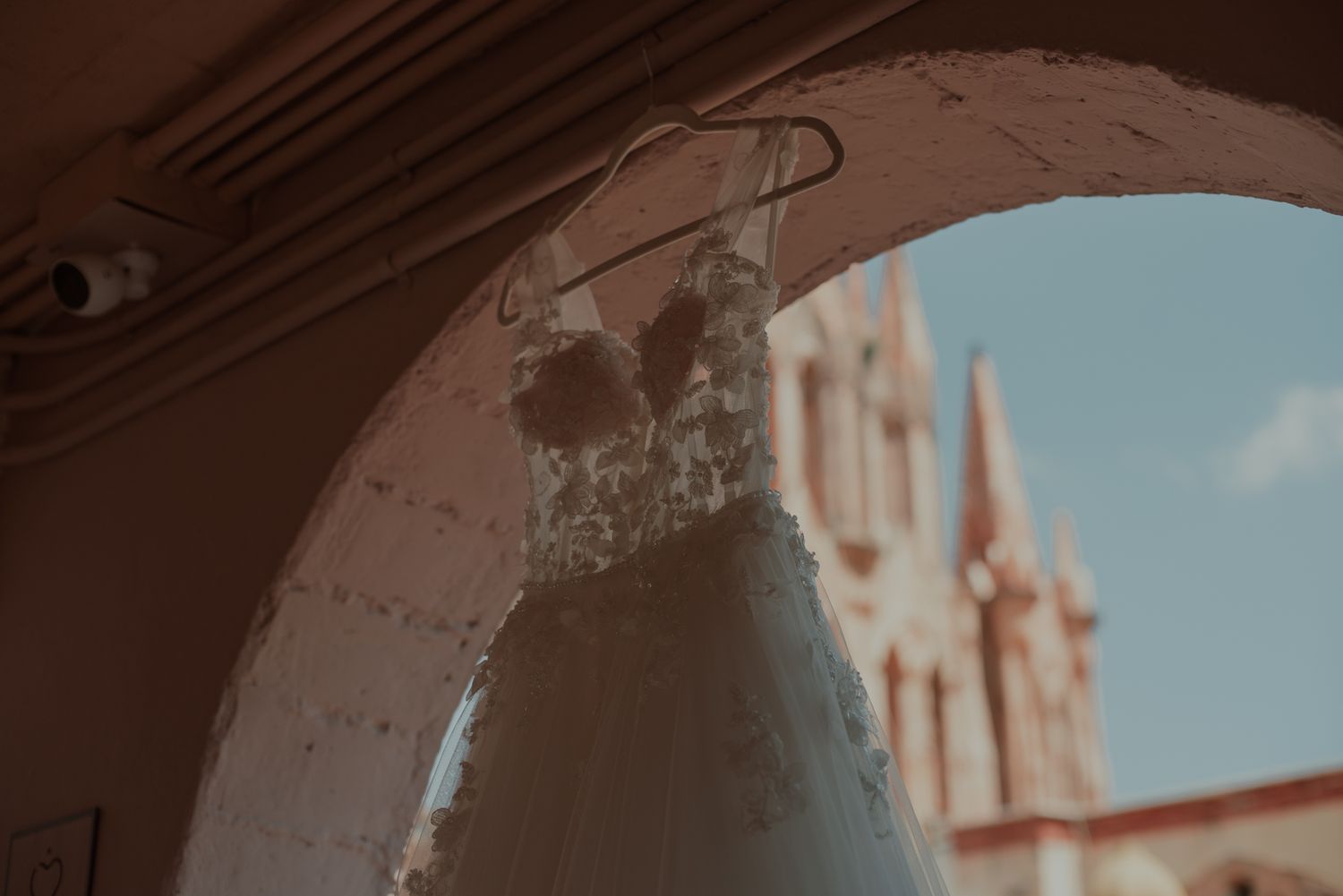 Close-up detail of a wedding dress with a church spire visible in the background.