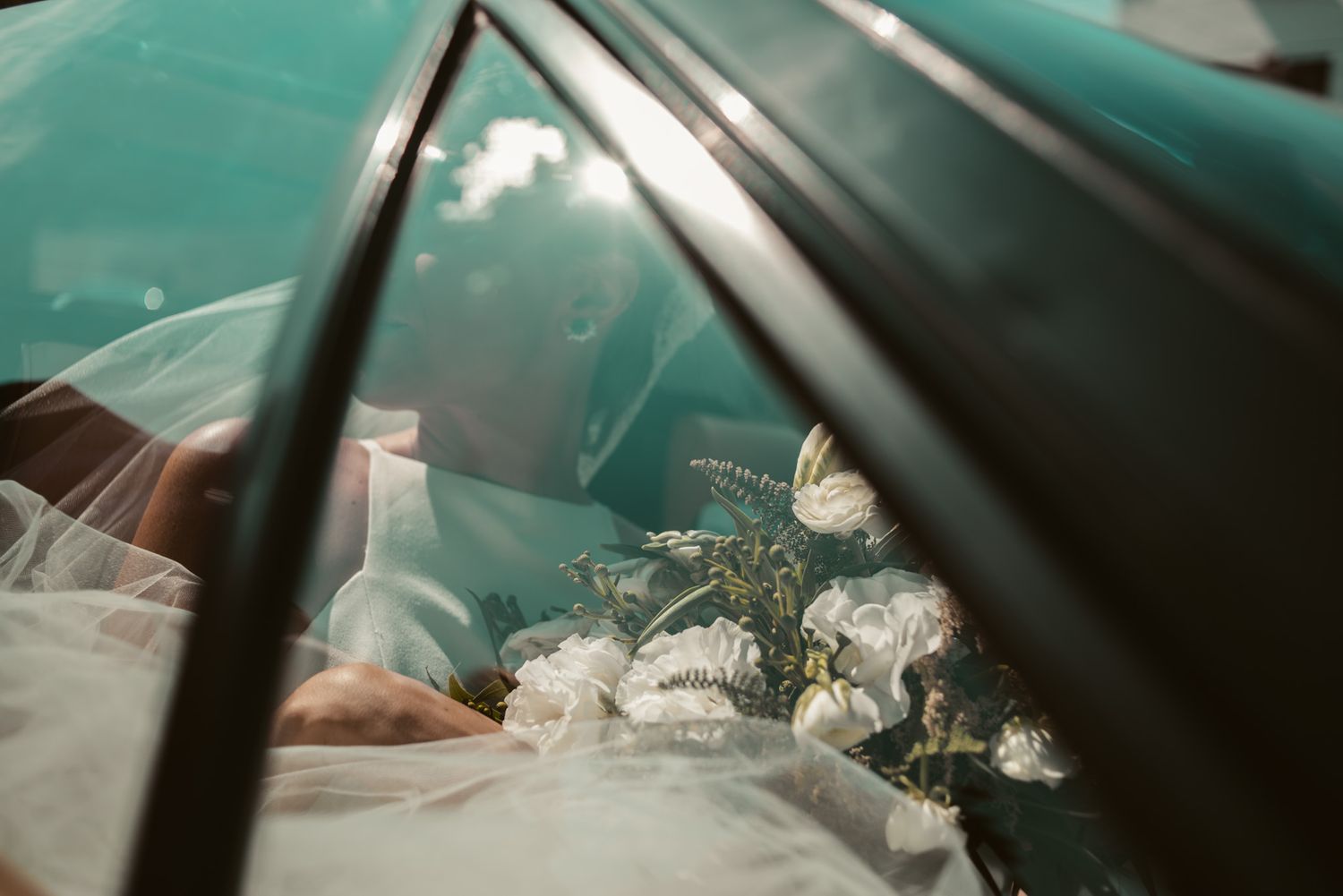 White flowers placed artistically in a car with turquoise interior seen through window reflections.