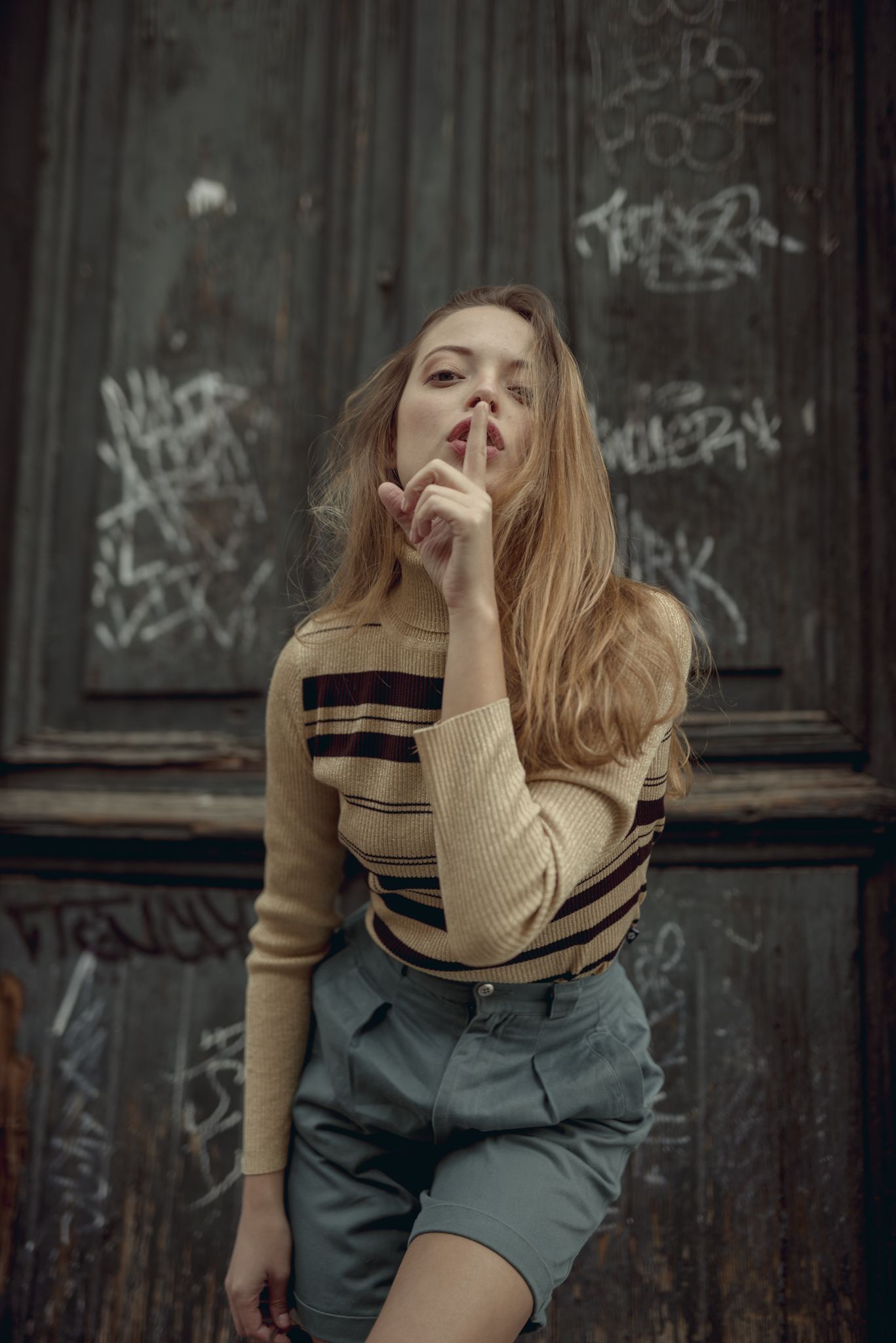 Urban fashion portrait against graffiti wall wearing striped sweater and shorts.