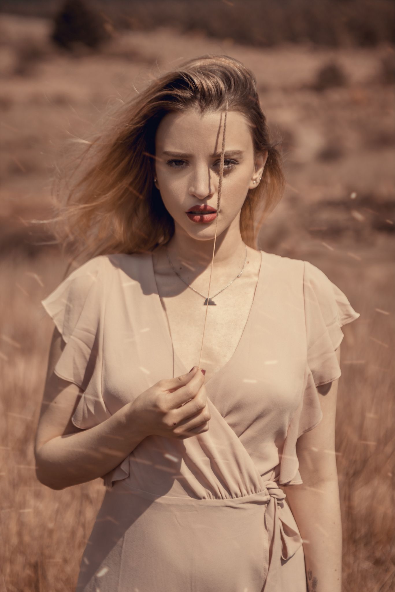 Ethereal portrait of woman in light dress standing in sepia-toned field.