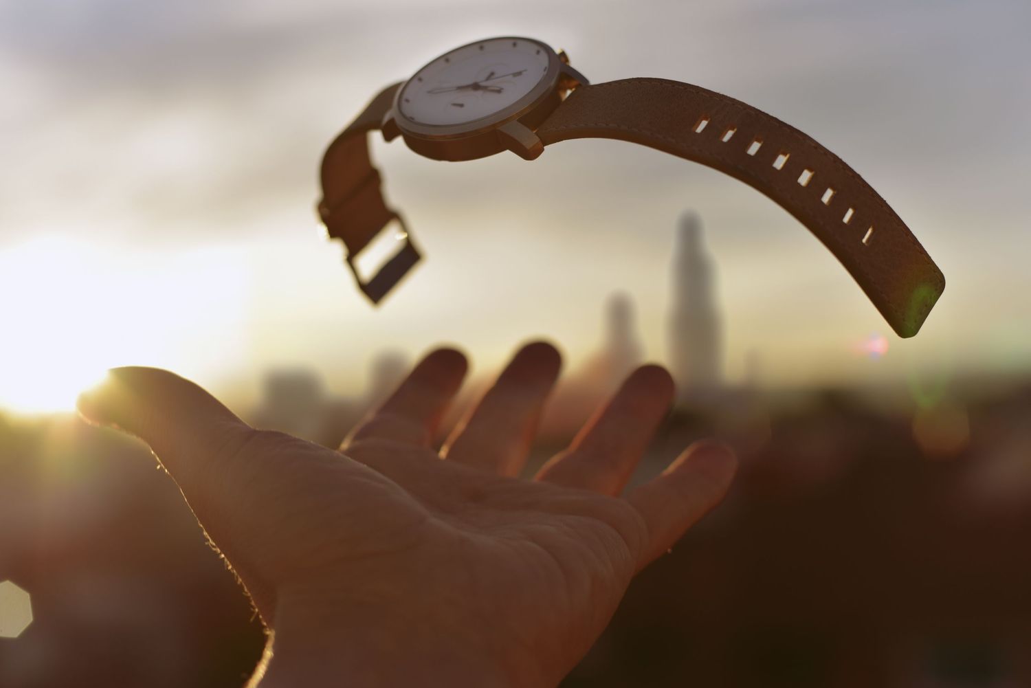 A floating wristwatch hovers over an outstretched hand silhouetted against a sunset city skyline.