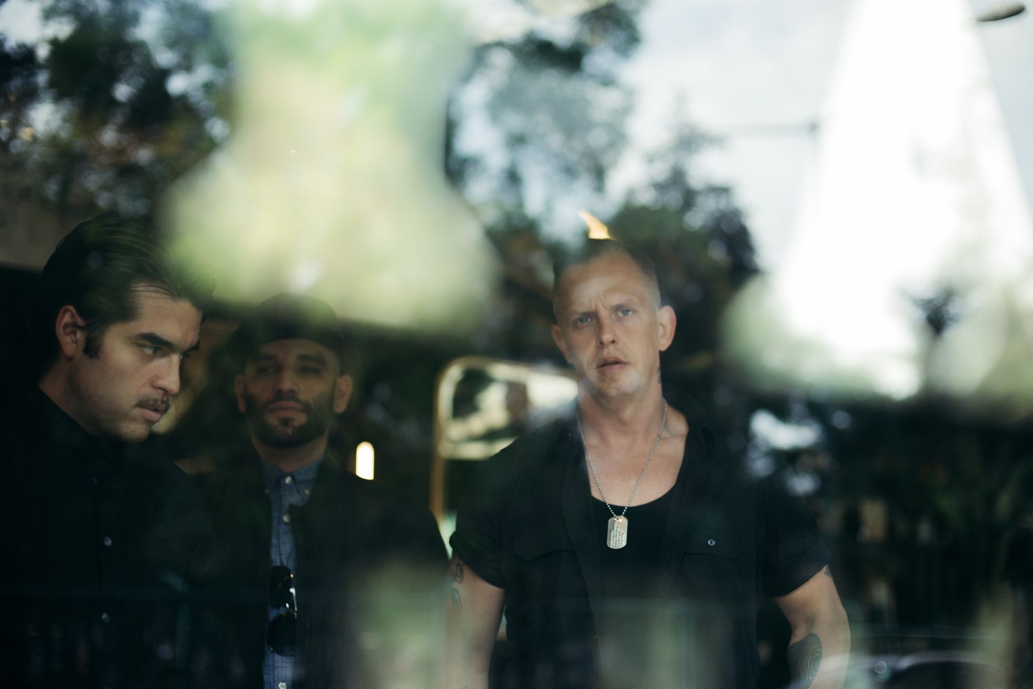 Three people in dark clothing photographed through reflective glass.