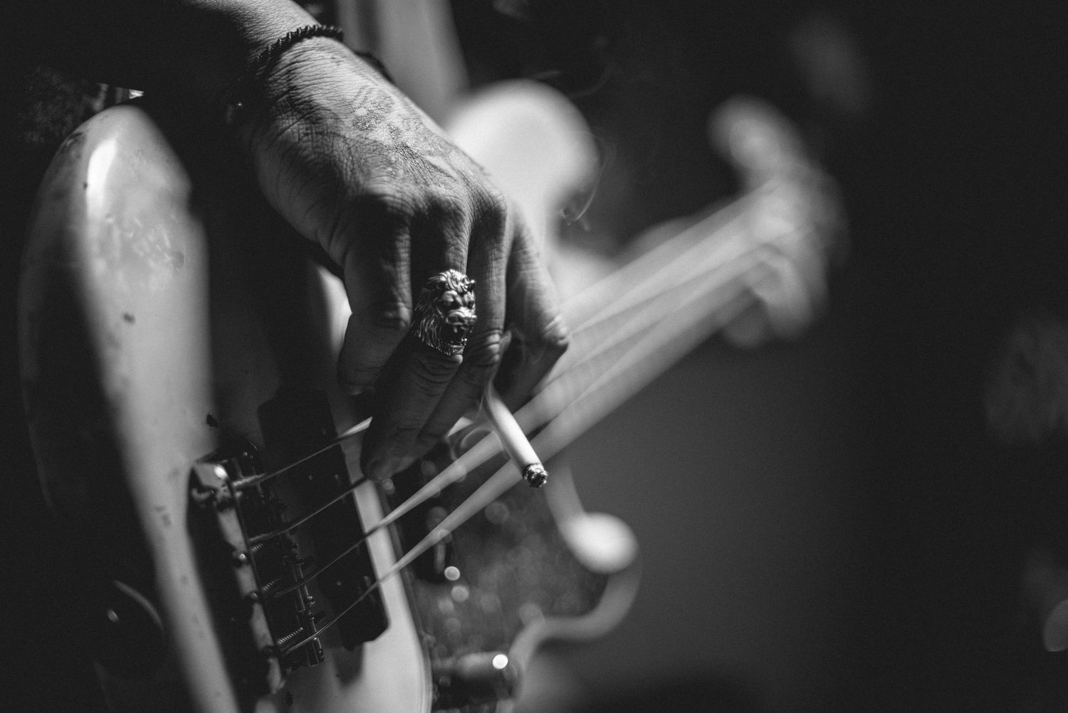 Dramatic black and white close-up of hands on bass guitar neck during performance.