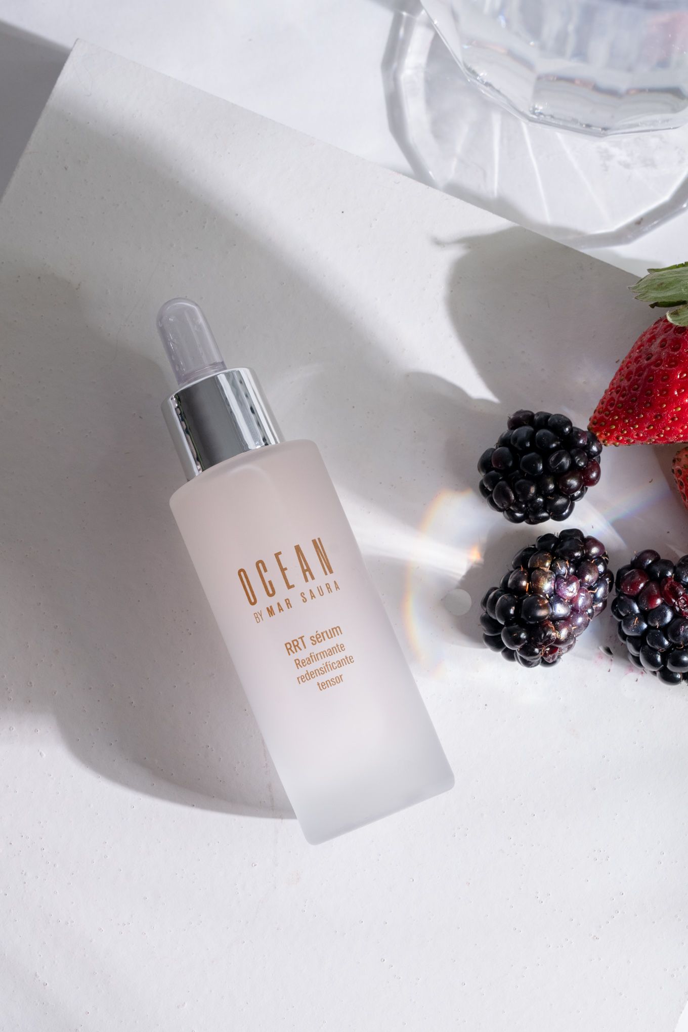 Ocean beauty serum bottle displayed with fresh blackberries and strawberry in natural light.