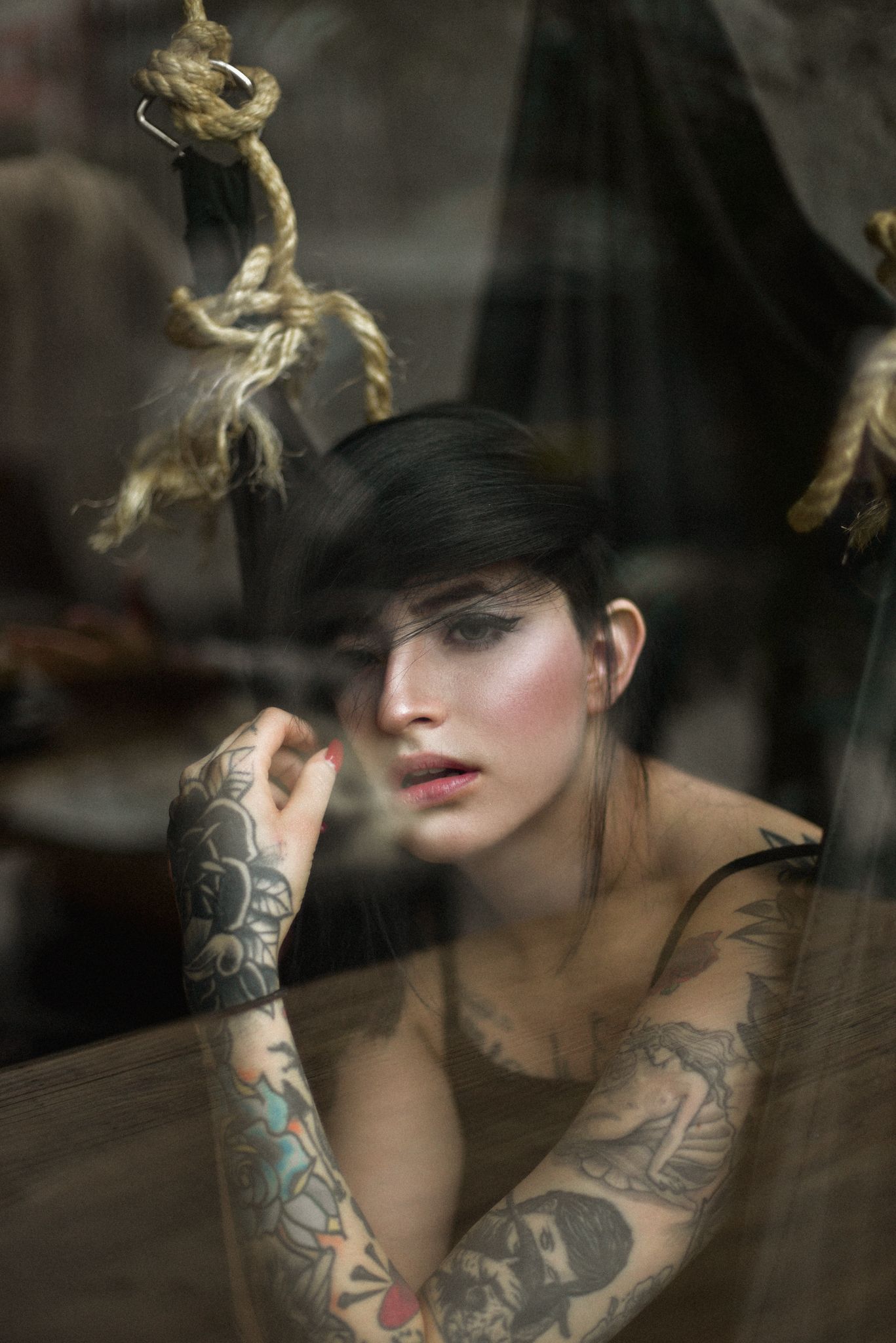 Person with visible tattoos poses artistically through glass with smoke effects.