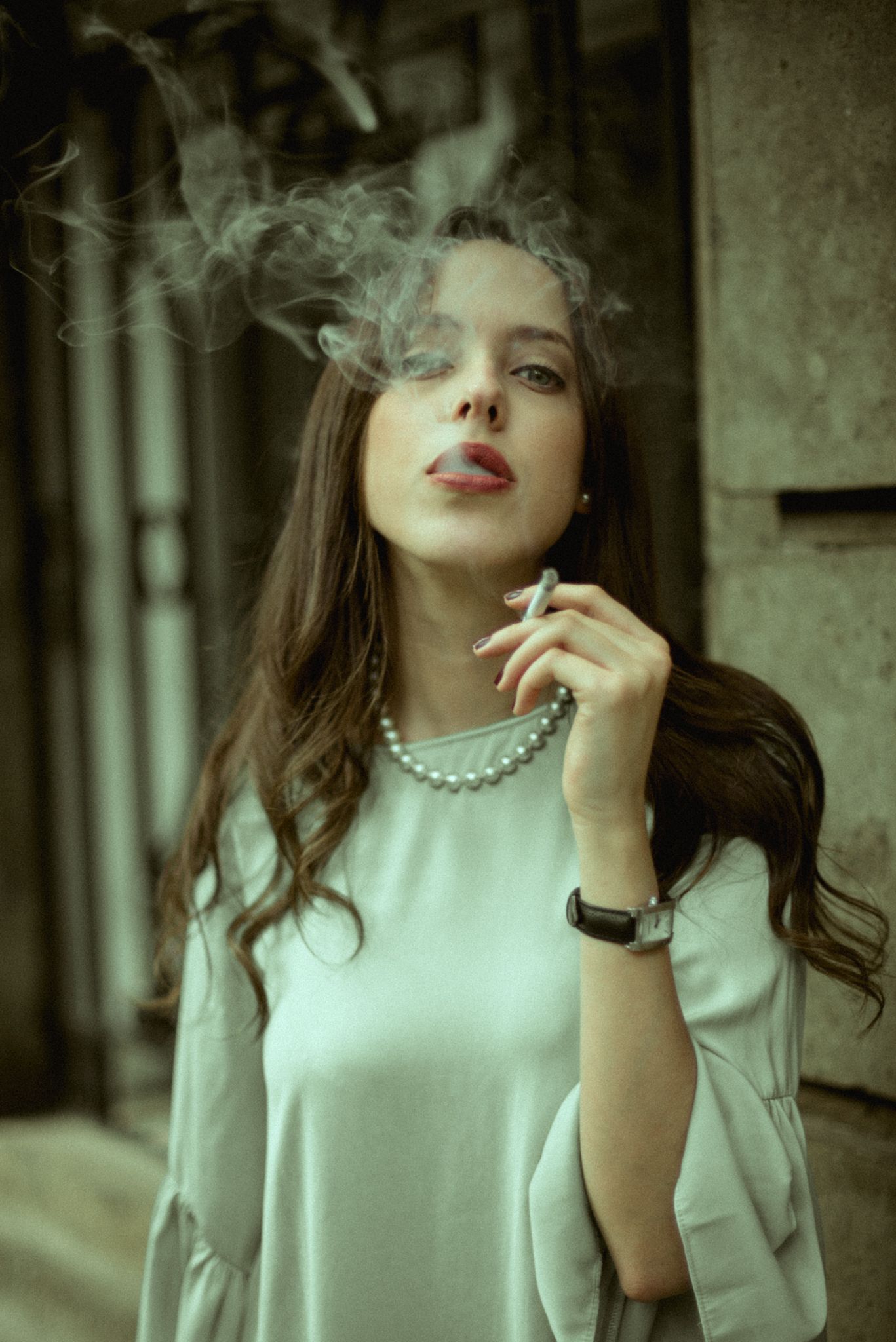 Vintage-inspired portrait with pearl necklace and cigarette smoke in muted tones.