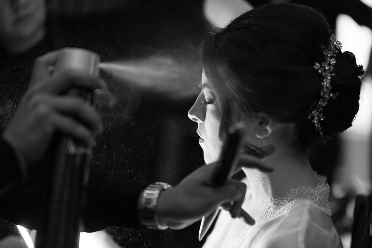 Artistic black and white photo of bride getting hair styled with spray.