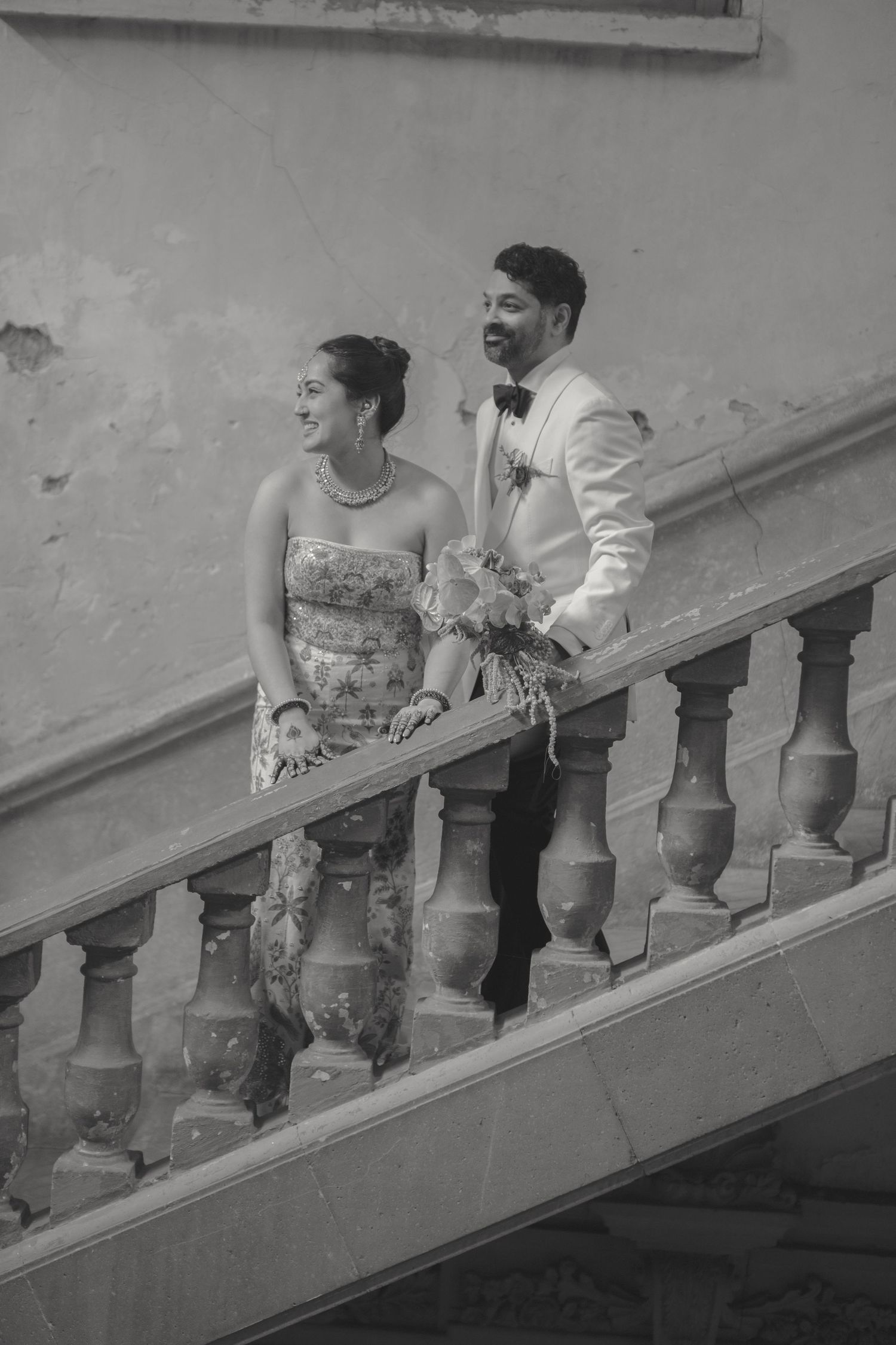 A couple shares a joyful moment on a historic staircase in formal wedding attire.