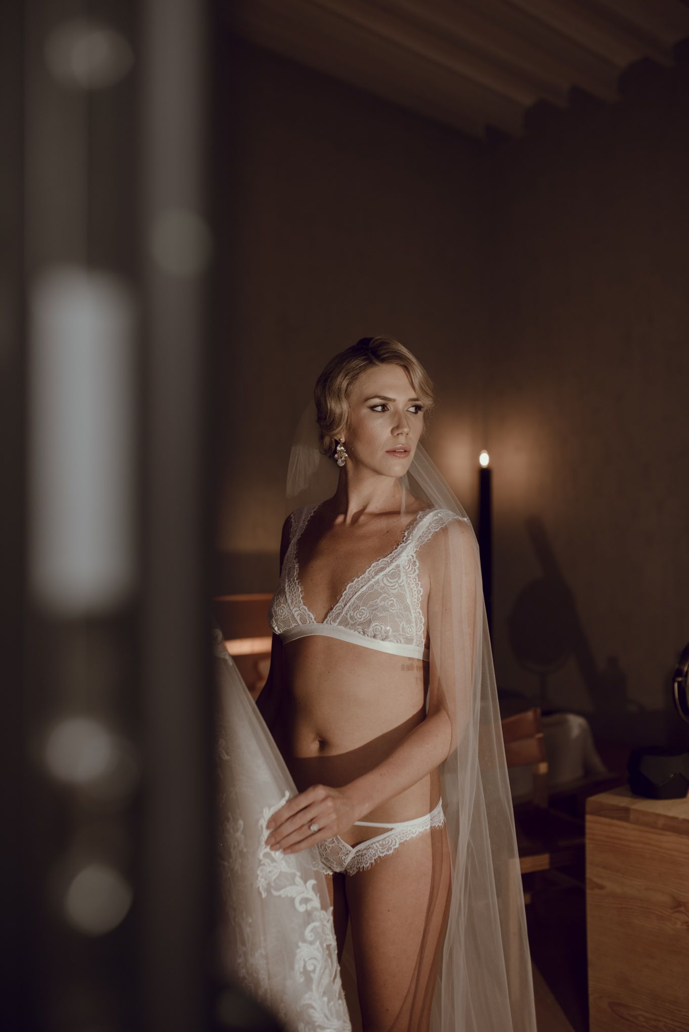 Moody boudoir portrait with candlelight and bridal accessories.