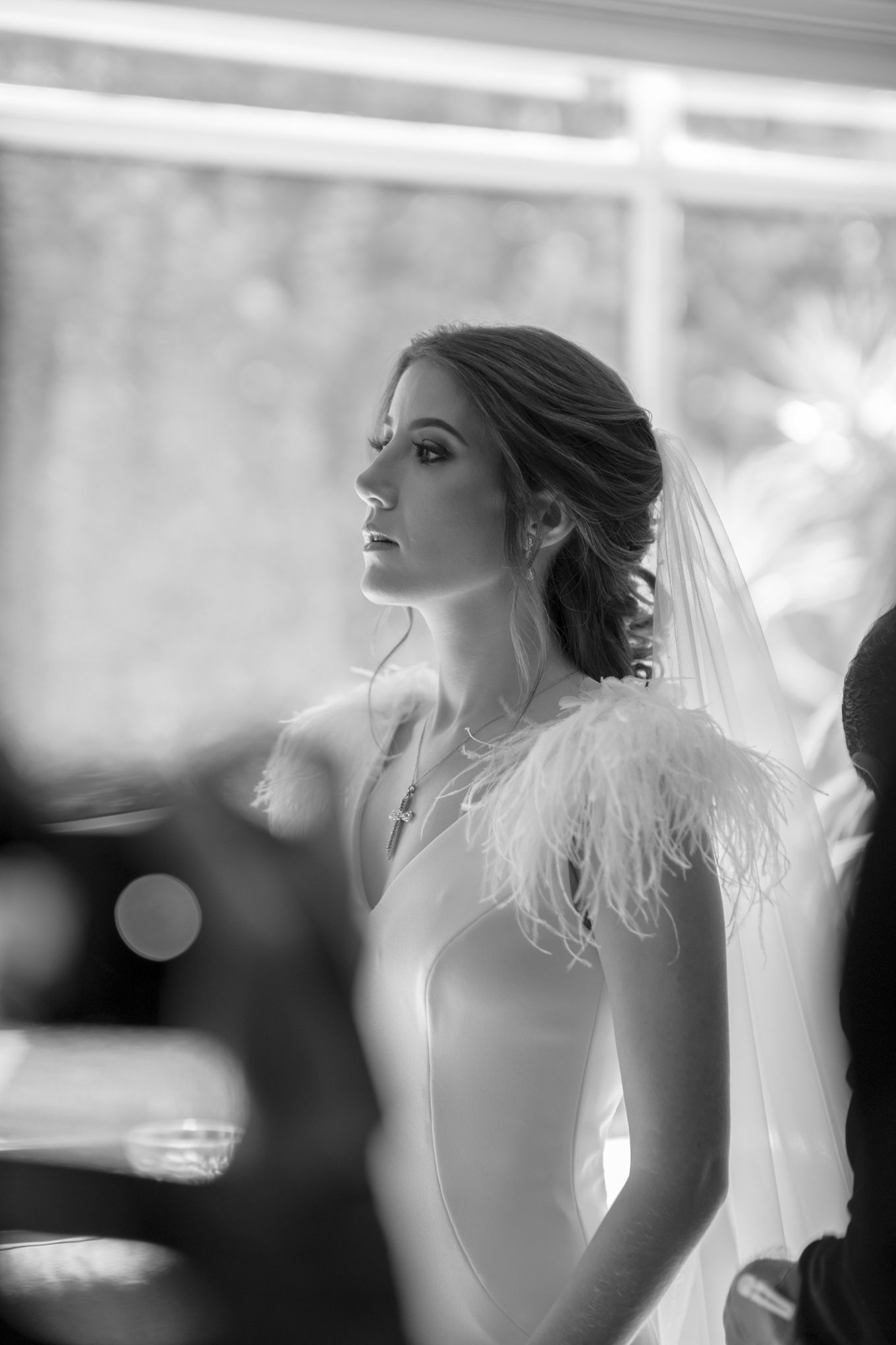 Profile view of a bride in an elegant white wedding dress adorned with a delicate feather detail and flowing veil.