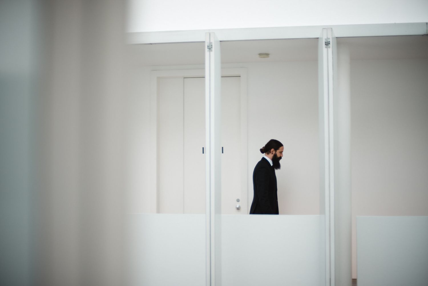 Silhouette of someone in black attire walking past white office partitions in a minimalist modern interior space.