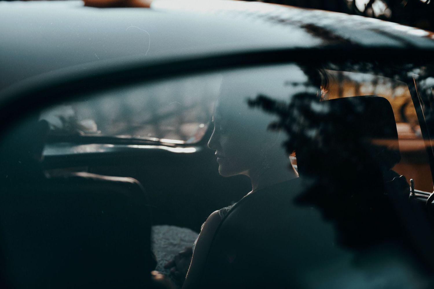 Silhouetted figure wearing hat visible through car window in moody dark lighting.