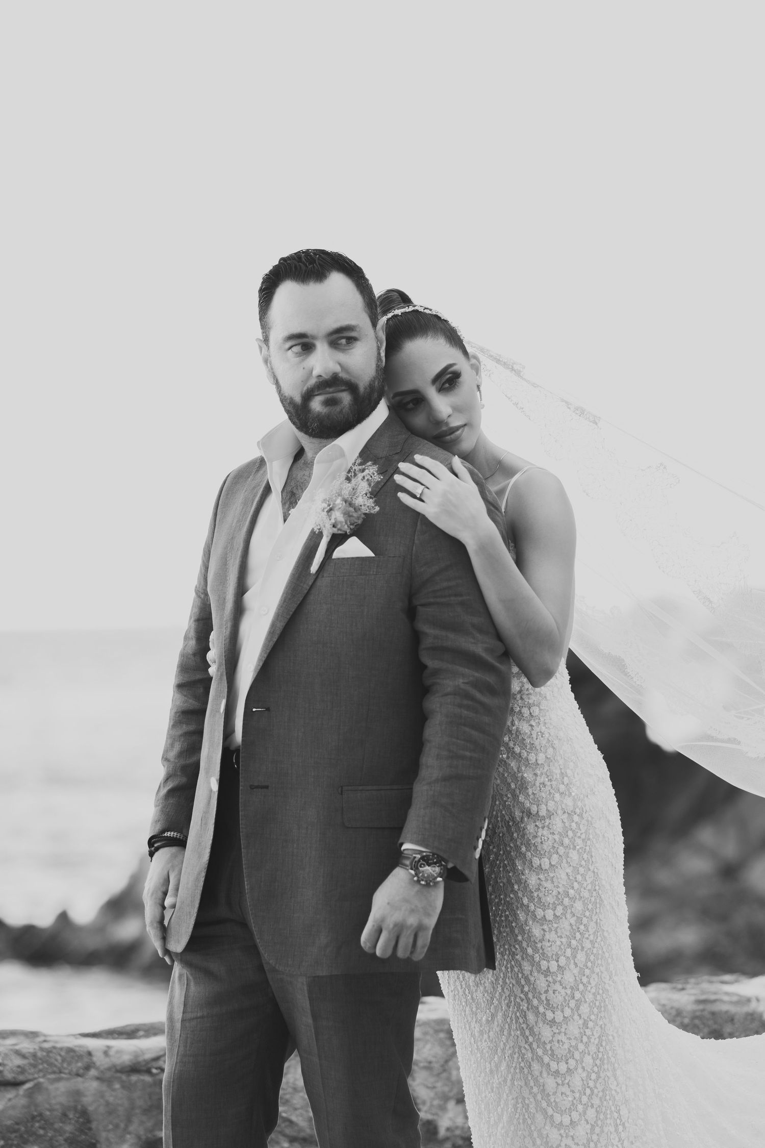 A black and white wedding portrait of a couple posing together against a cloudy sky.
